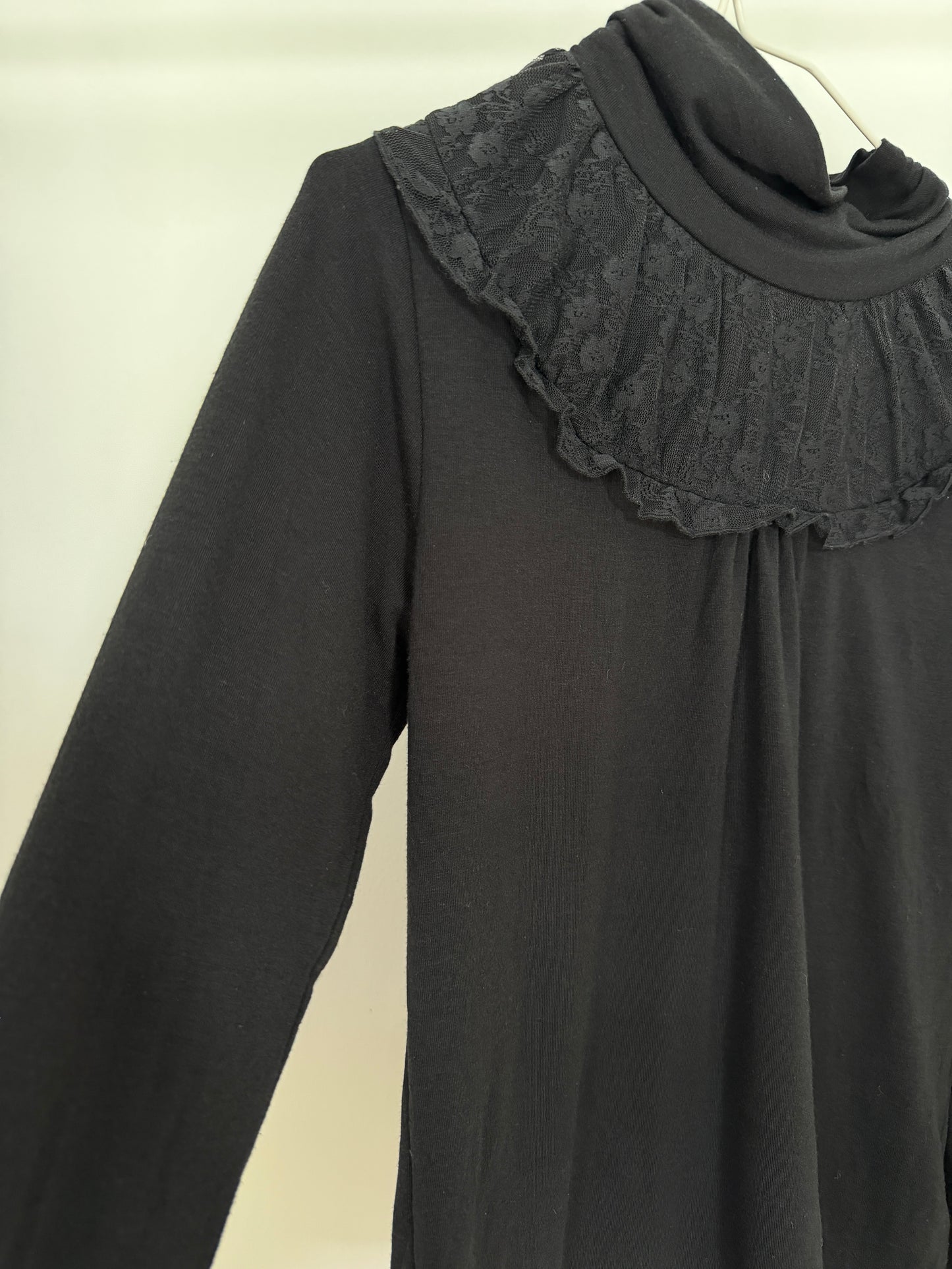 A black long-sleeve top with a wide, ruffled lace collar, shown hanging against a plain light background.