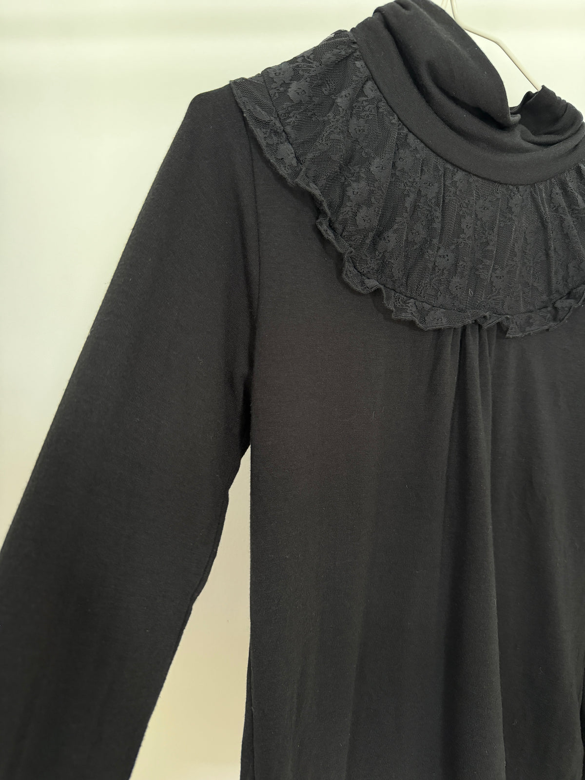 A black long-sleeve top with a wide, ruffled lace collar, shown hanging against a plain light background.