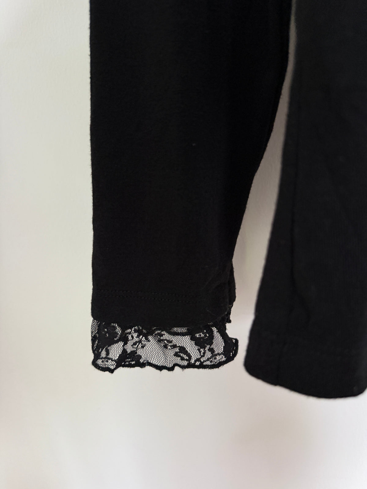 Lace trim at the cuffs, hanging against a plain off-white background.