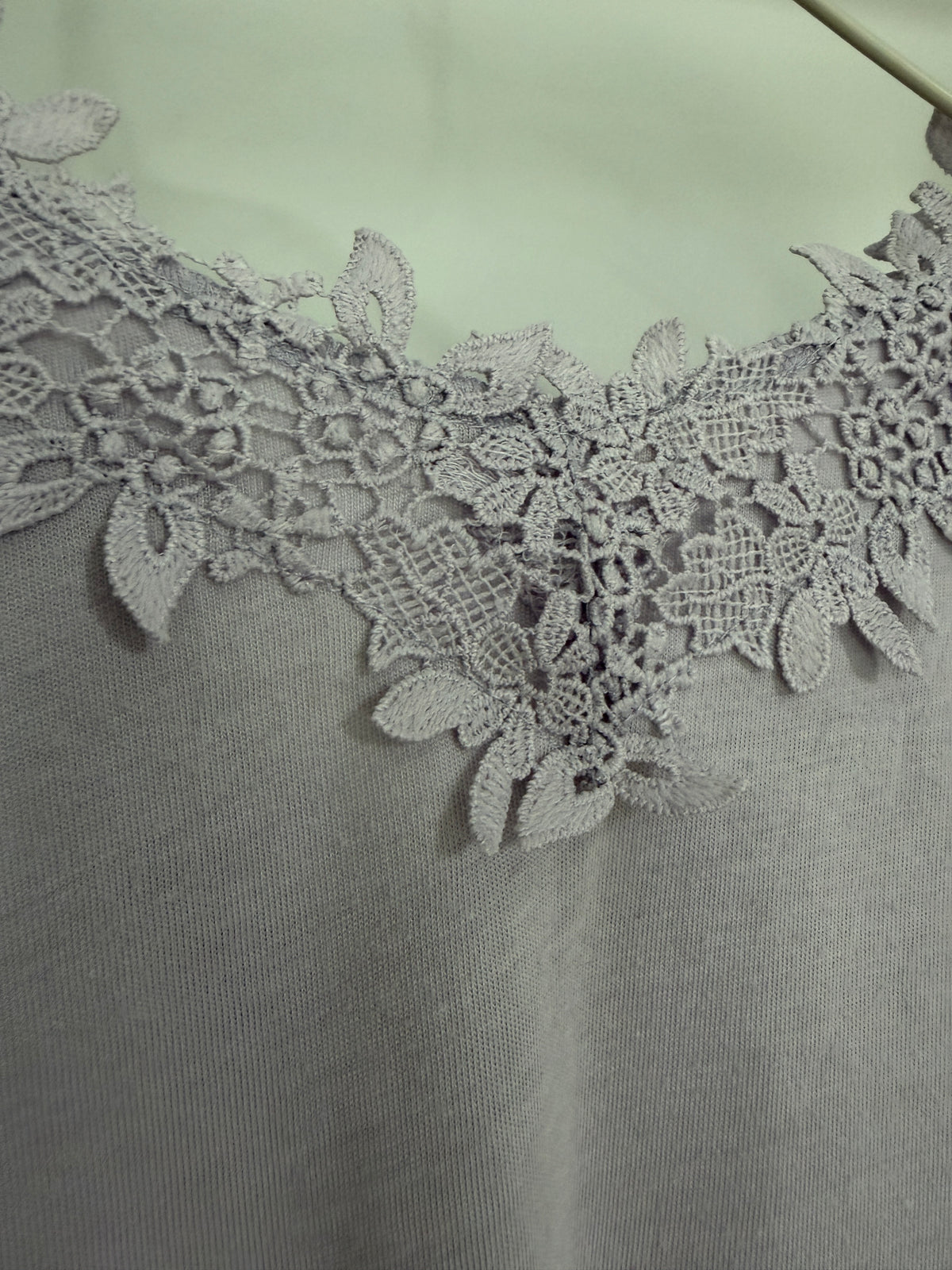 Close-up of a light gray knit top featuring an intricate floral lace collar in a matching gray shade.