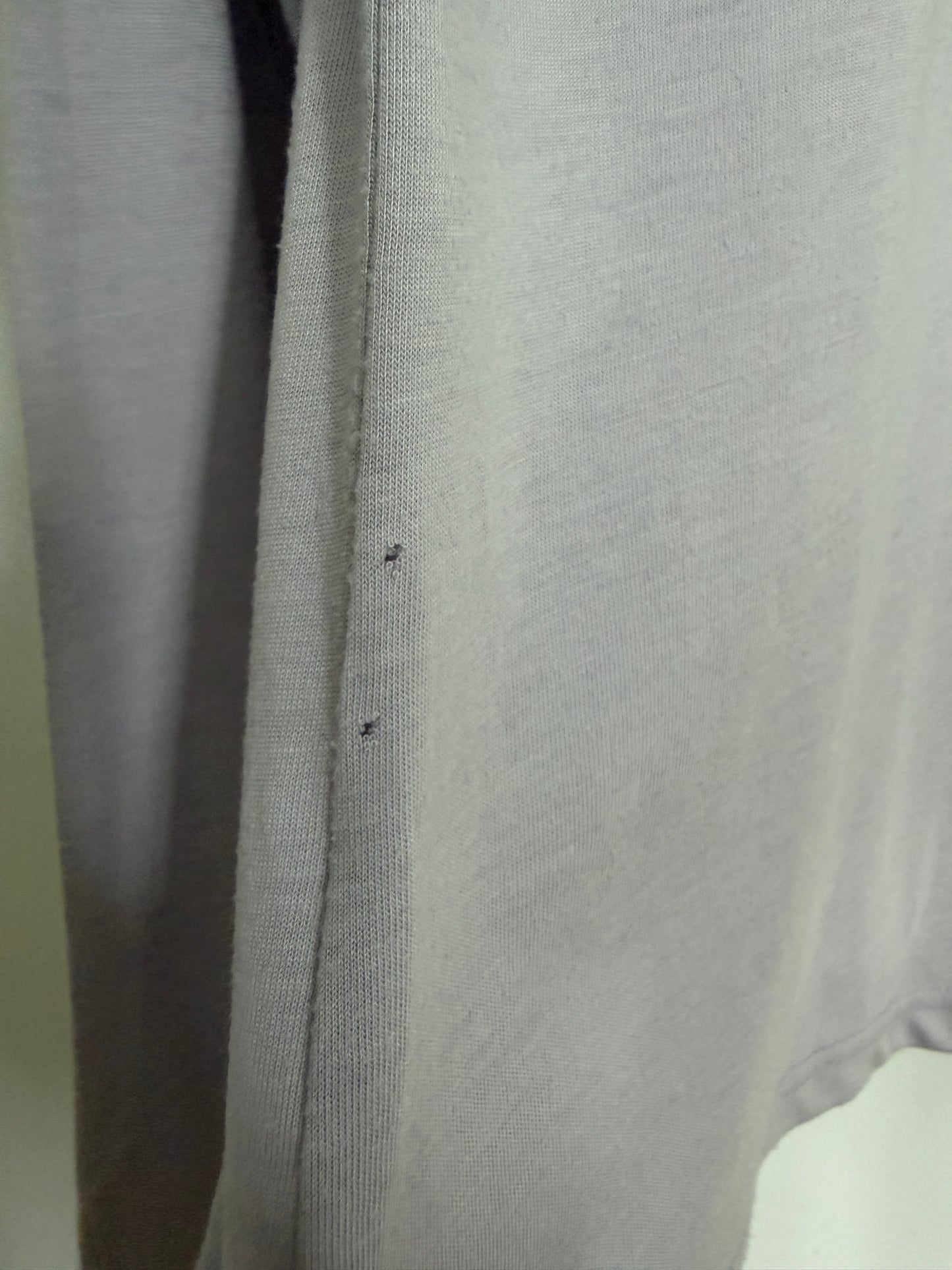 Close-up of a light gray knit fabric garment, showing the texture and a small dark defect or stain on the side seam.