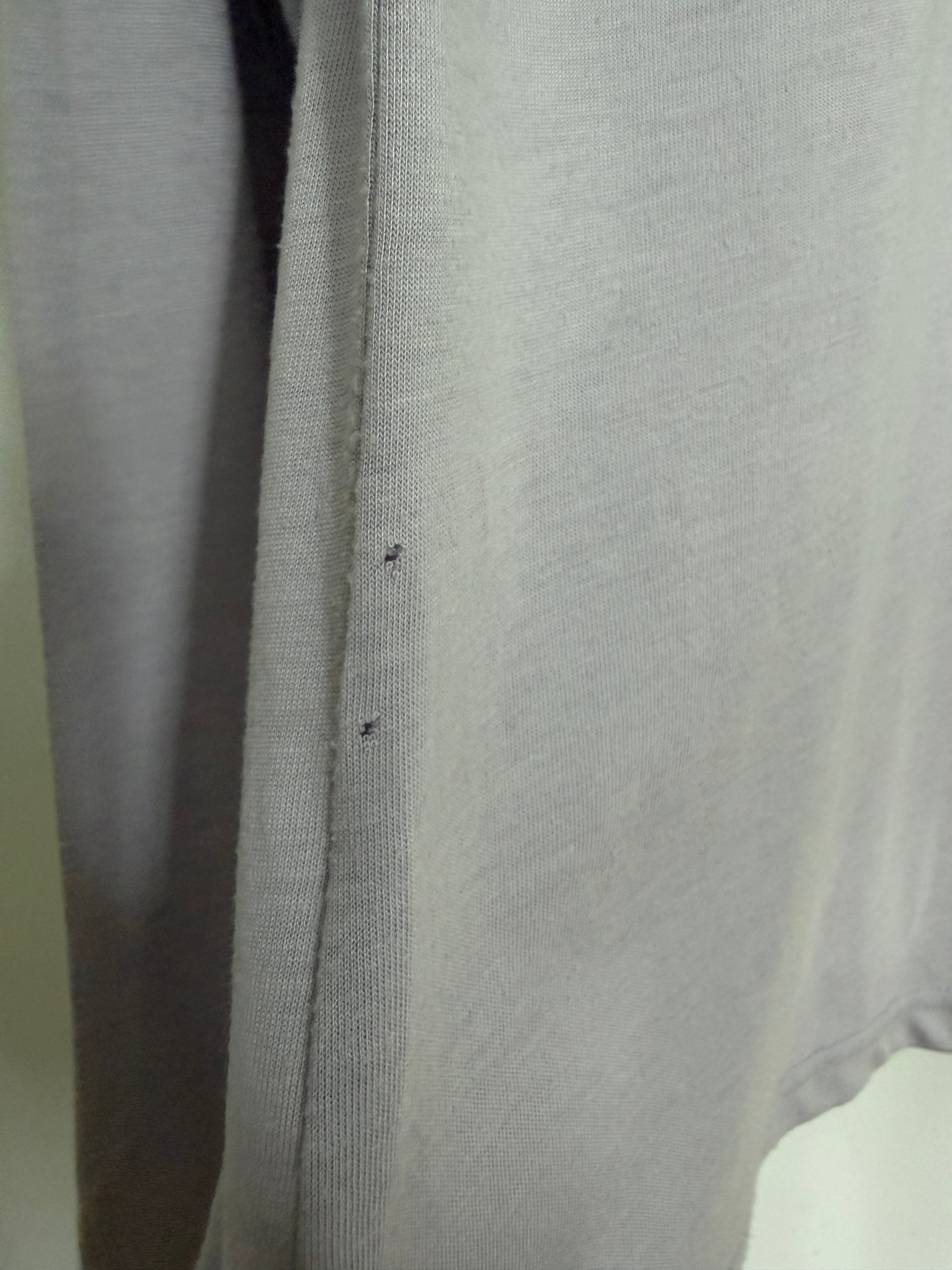 Close-up of a light gray knit fabric garment, showing the texture and a small dark defect or stain on the side seam.