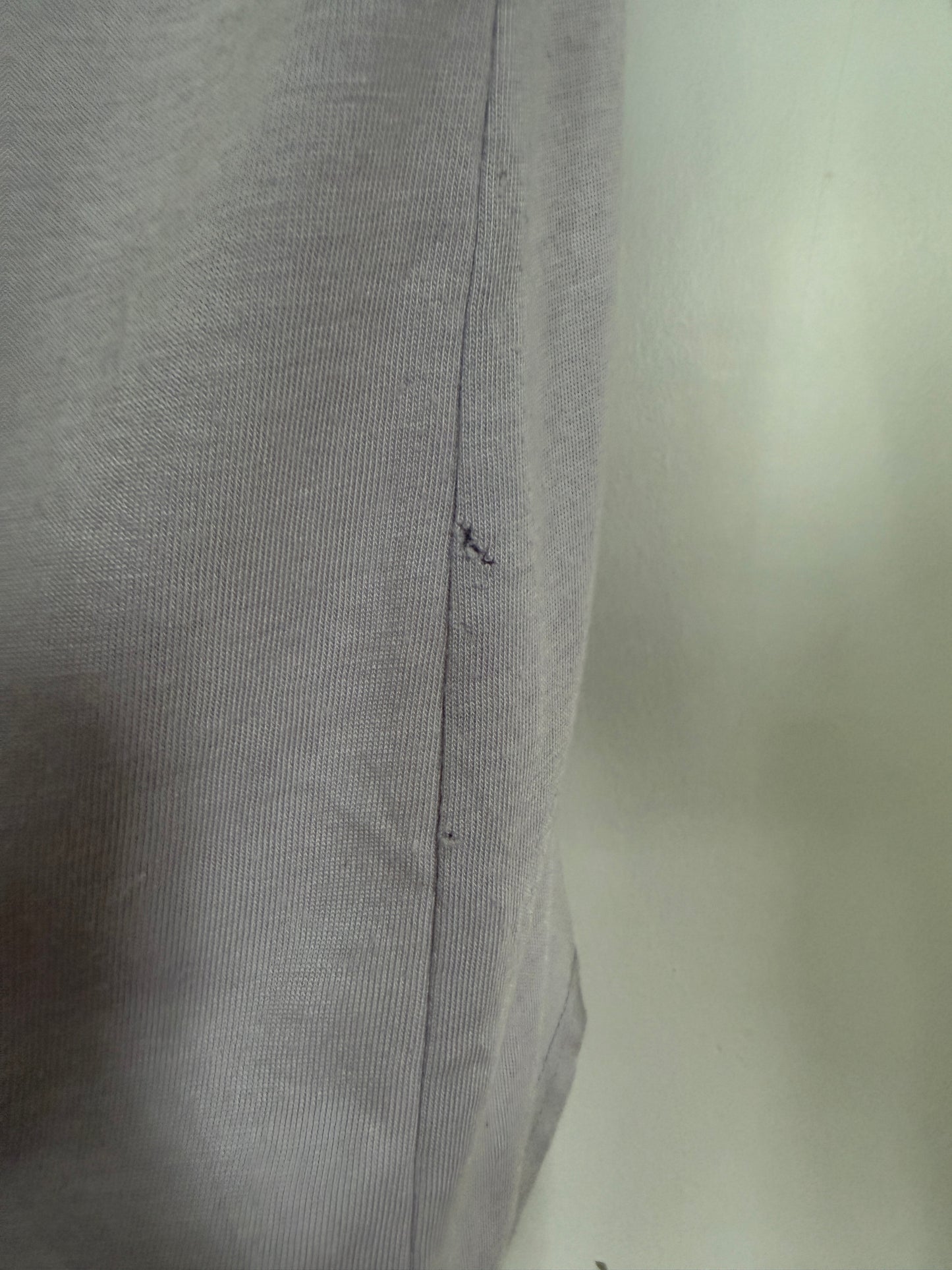 Close-up of a light gray ribbed fabric with a vertical seam and a small dark mark near the center, photographed against a pale background.