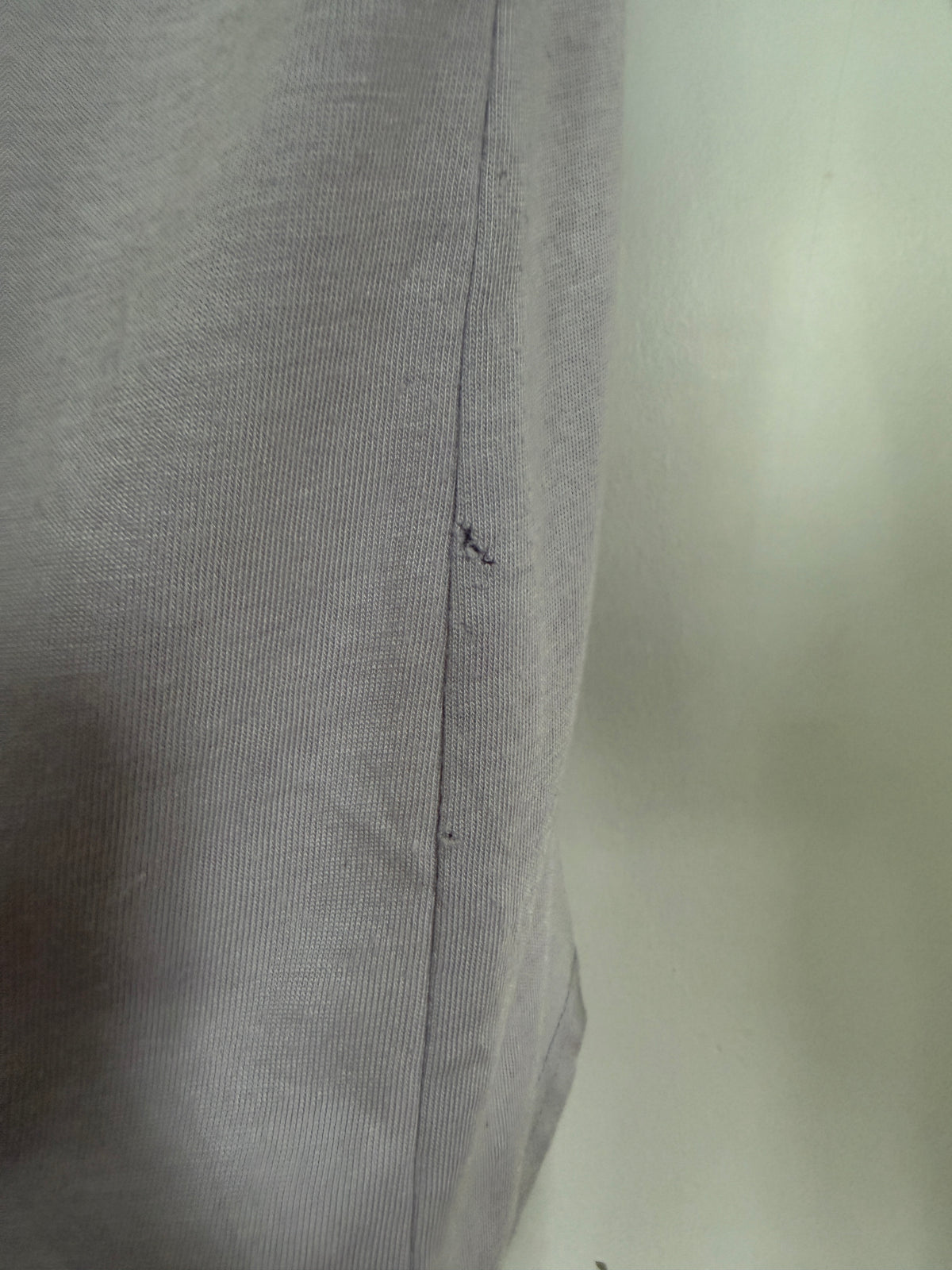 Close-up of a light gray ribbed fabric with a vertical seam and a small dark mark near the center, photographed against a pale background.