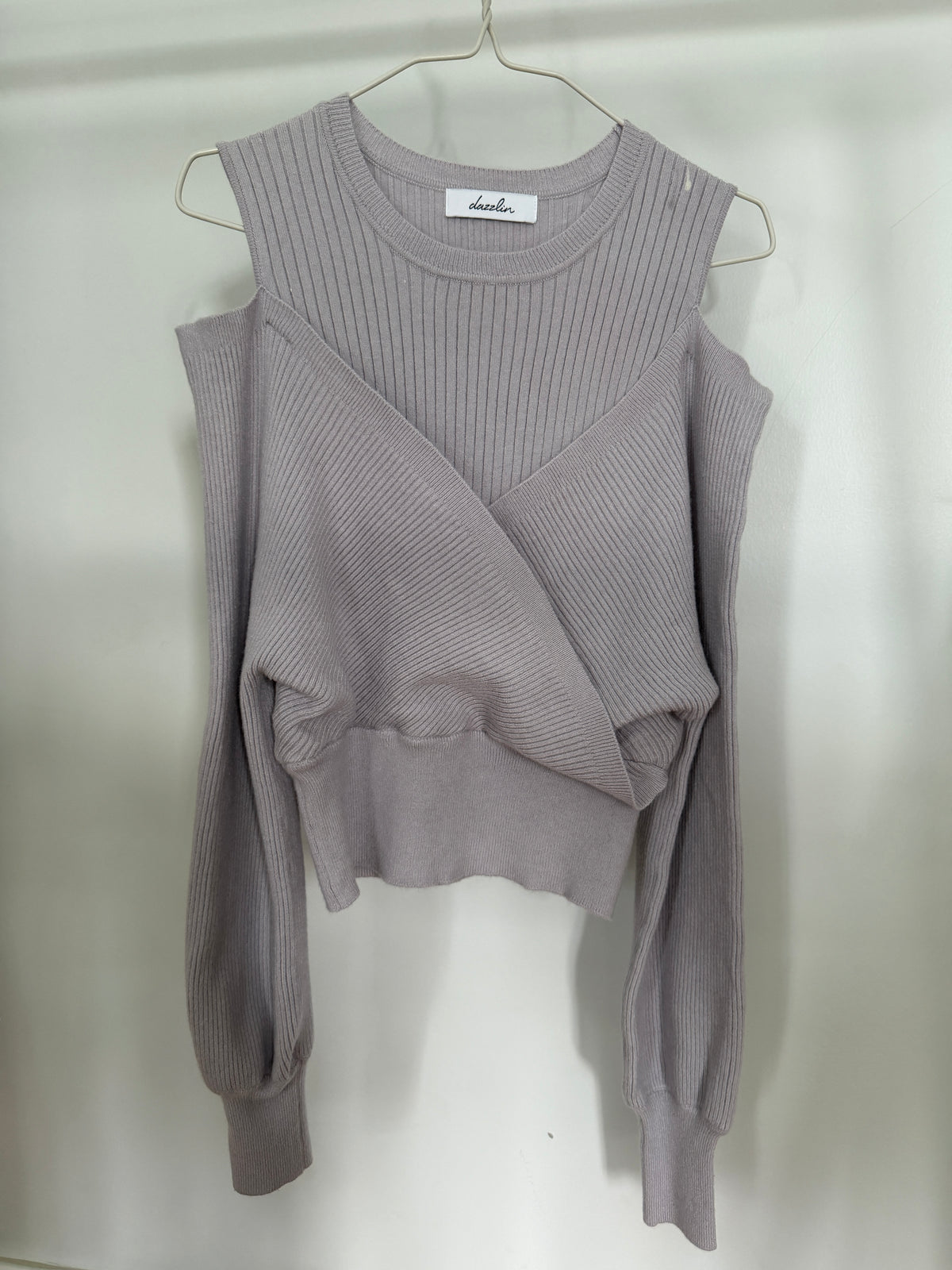 A light gray ribbed knit sweater with a crew neck, long sleeves, and a wrap-style crossover front, hanging on a metal hanger against a plain light background.