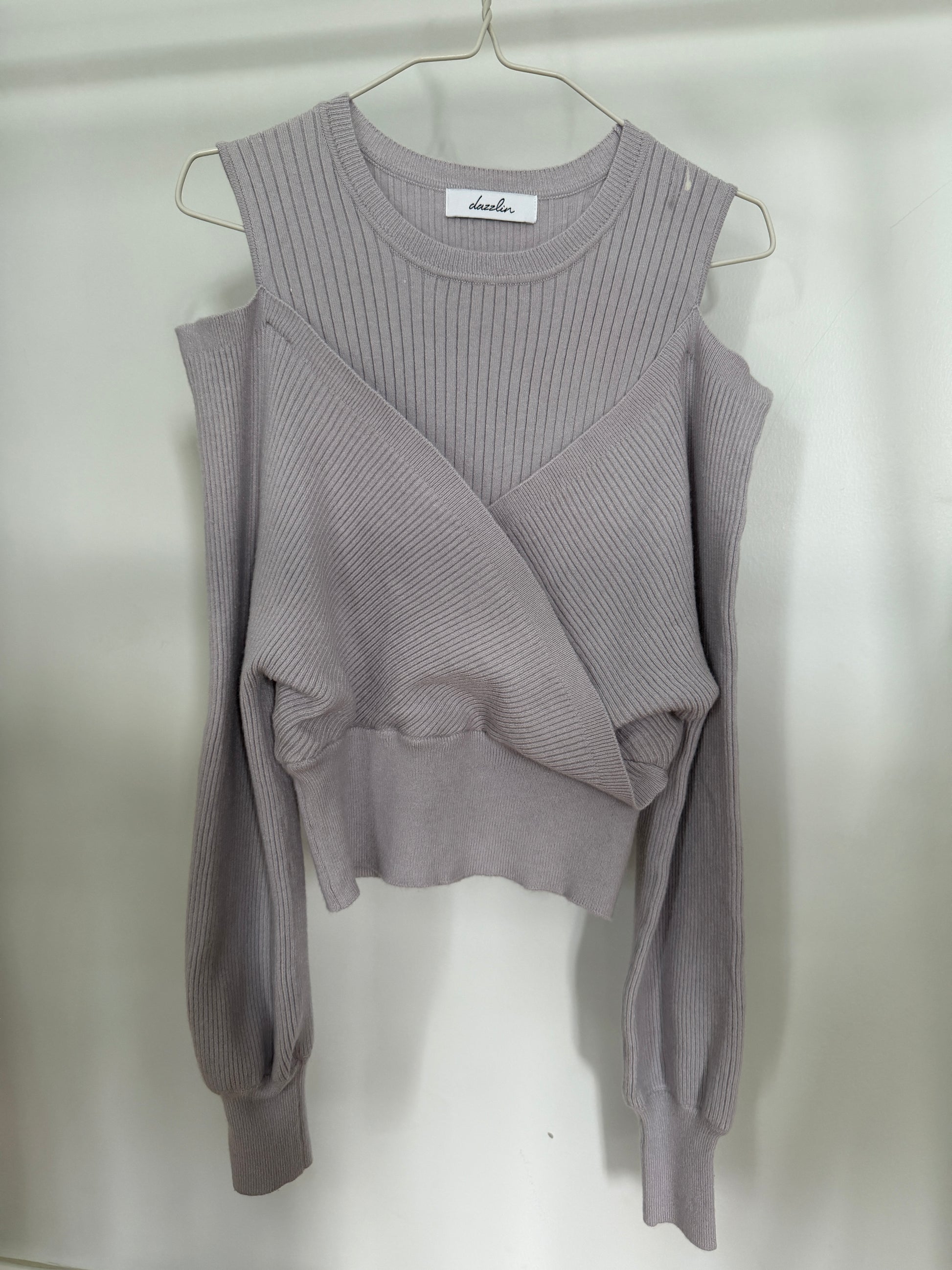 A light gray ribbed knit sweater with a crew neck, long sleeves, and a wrap-style crossover front, hanging on a metal hanger against a plain light background.