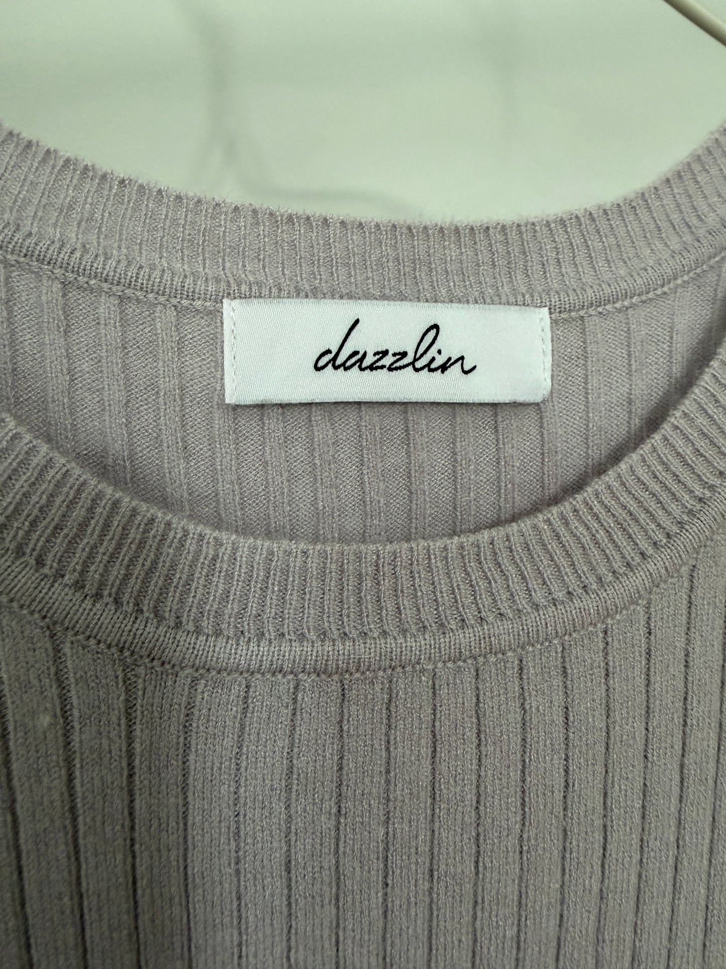 Close-up of a ribbed knit top with a white neck label reading 'dazzlin' in black script.
