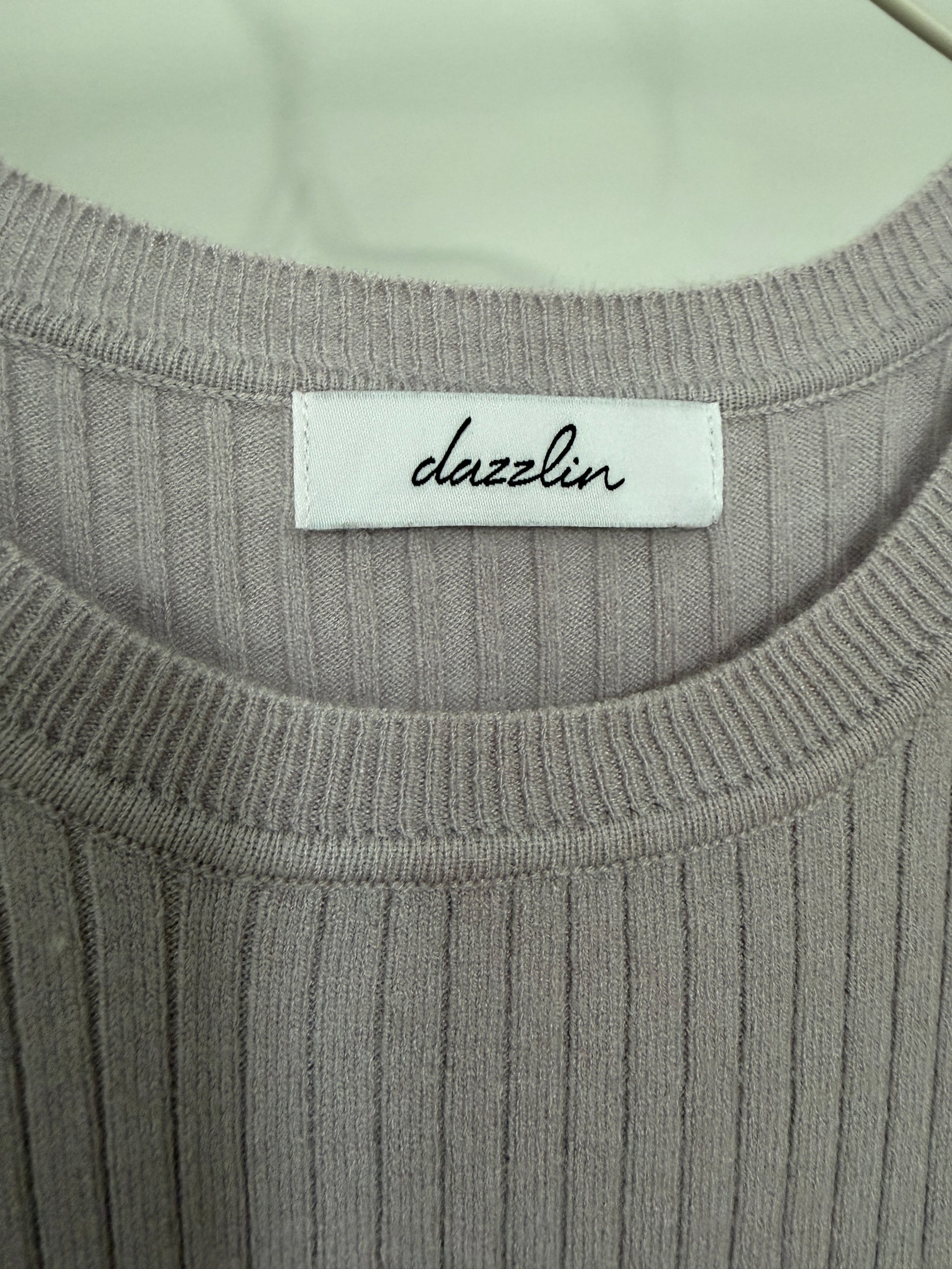 Close-up of a ribbed knit top with a white neck label reading 'dazzlin' in black script.