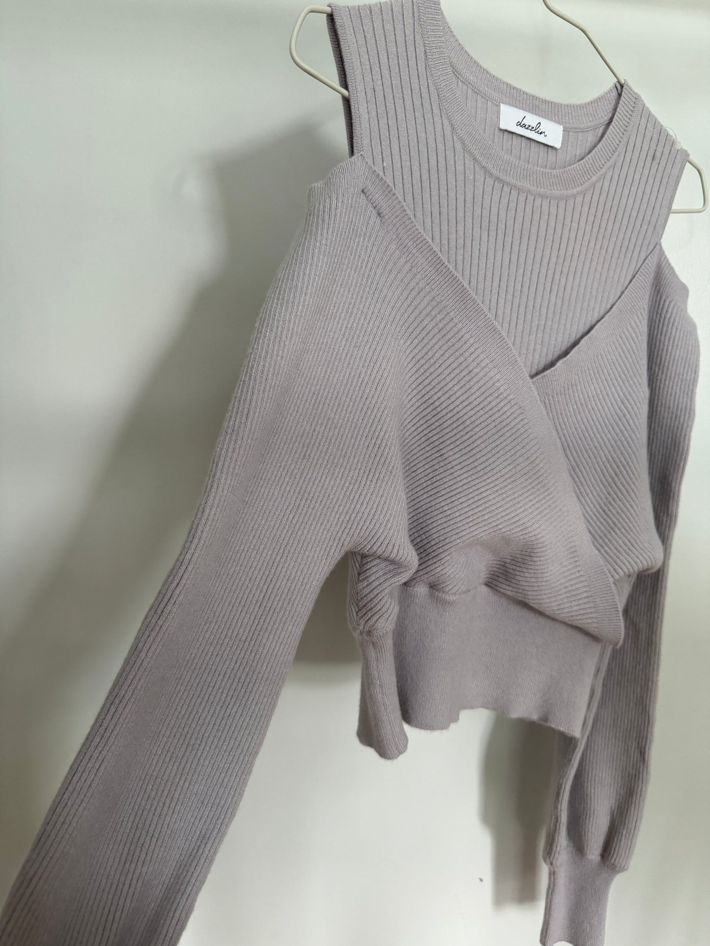 A light gray ribbed knit long-sleeve top with a wrap-style crossover front, hanging on a metal hanger against a plain light background.