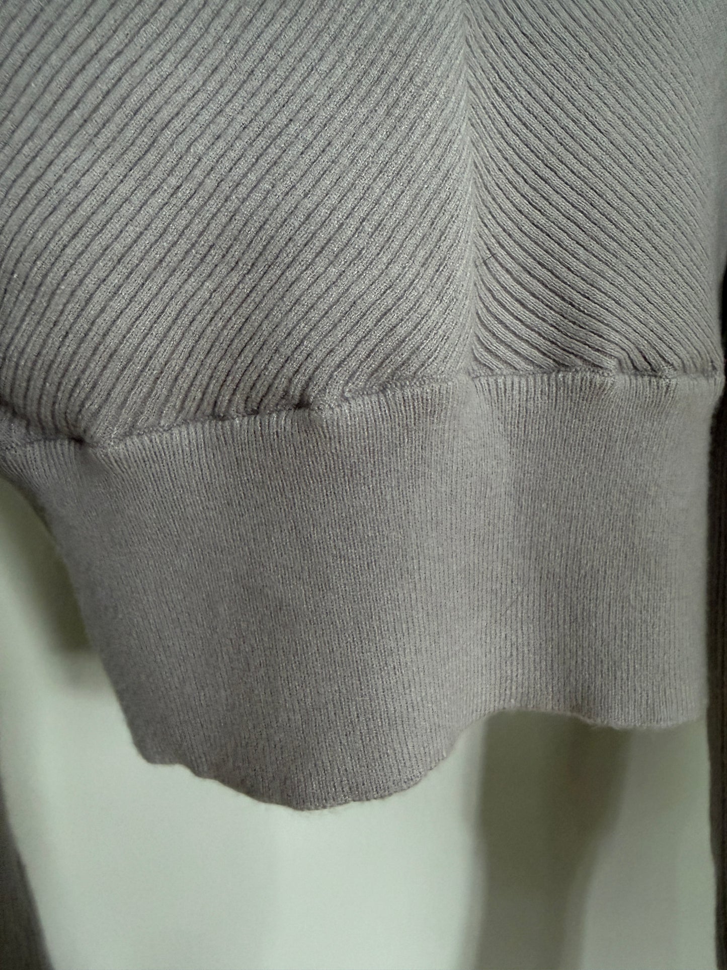 Close-up of a light gray ribbed knit garment, showing the sleeve cuff and textured fabric detail.