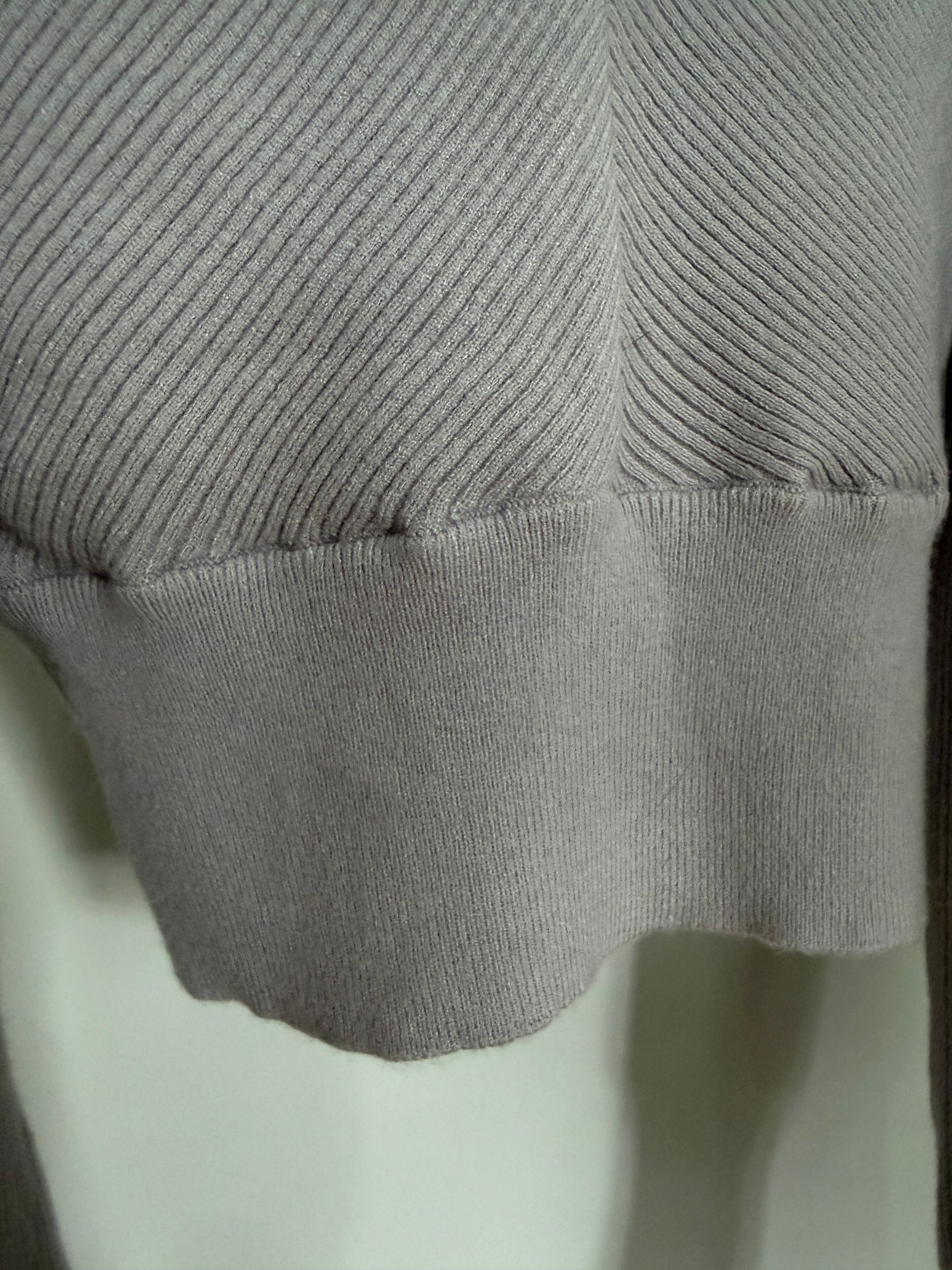 Close-up of a light gray ribbed knit garment, showing the sleeve cuff and textured fabric detail.