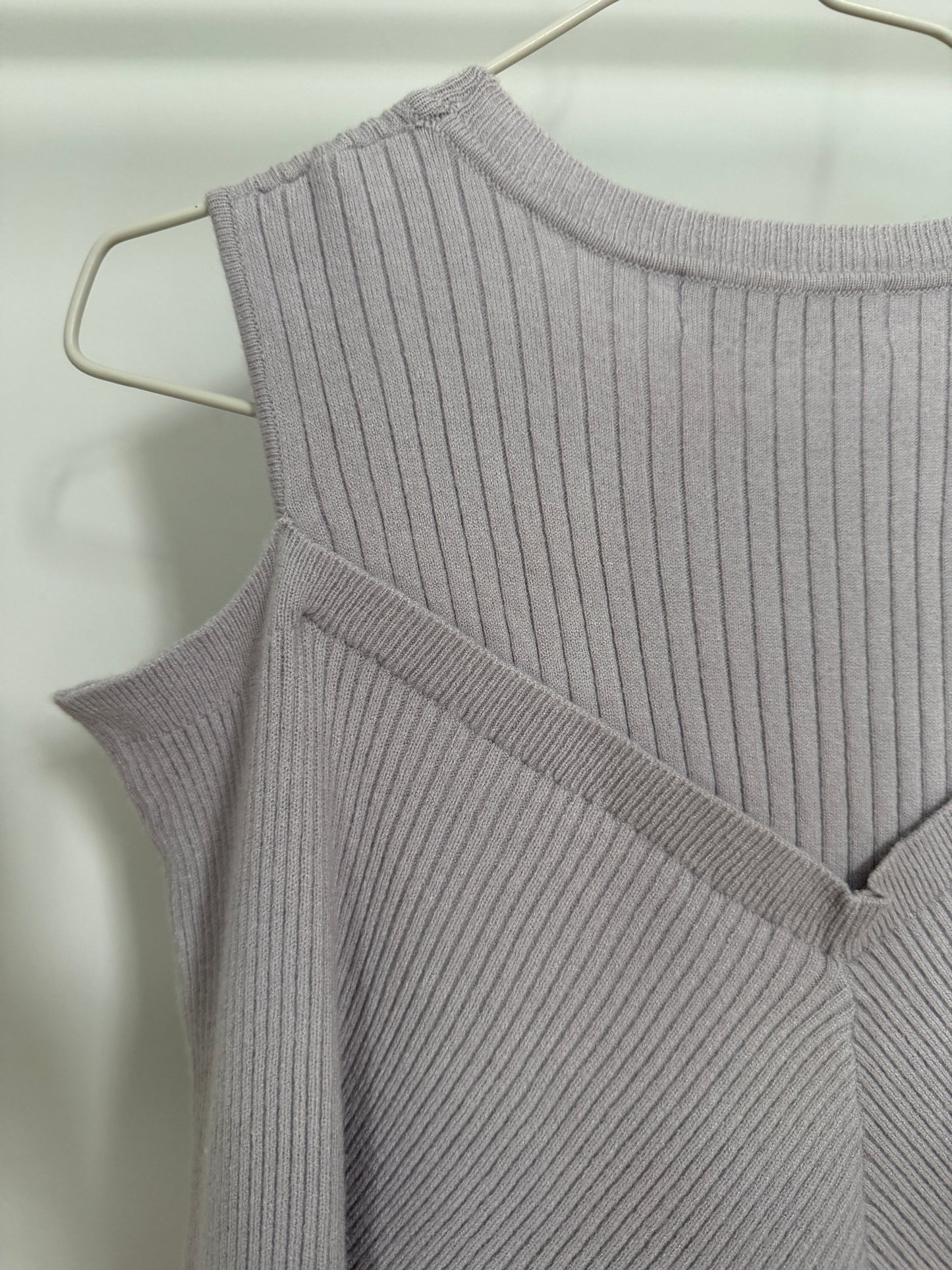 A close-up of a light gray ribbed knit sleeveless top hanging on a white wire hanger against a plain light background.
