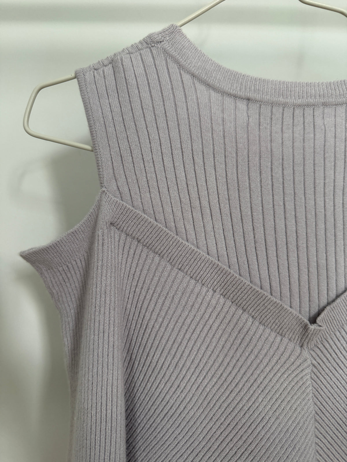 A close-up of a light gray ribbed knit sleeveless top hanging on a white wire hanger against a plain light background.