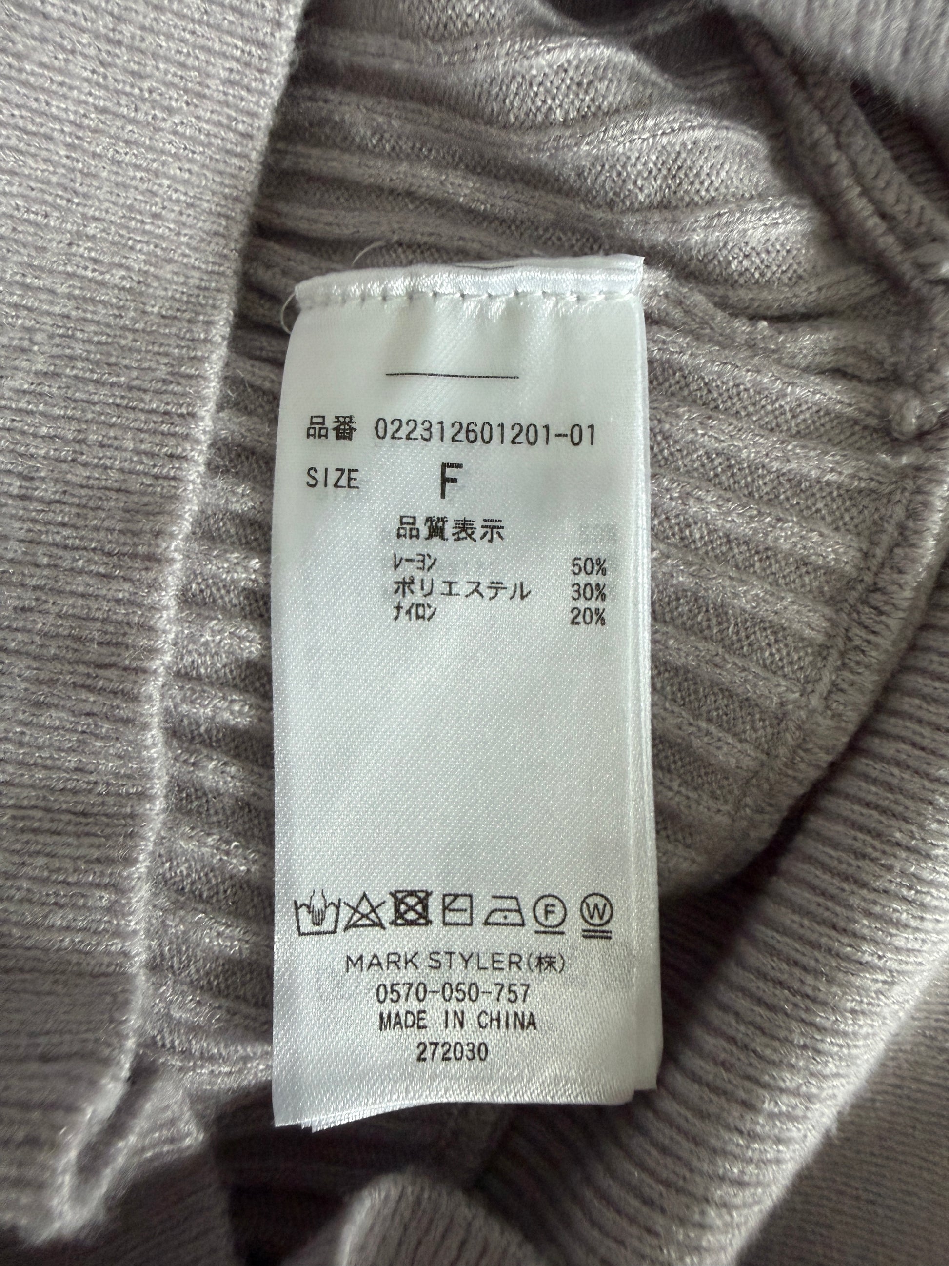 Close-up of a white garment care label sewn onto the inside neck of a ribbed gray knit sweater, showing size F and care symbols.