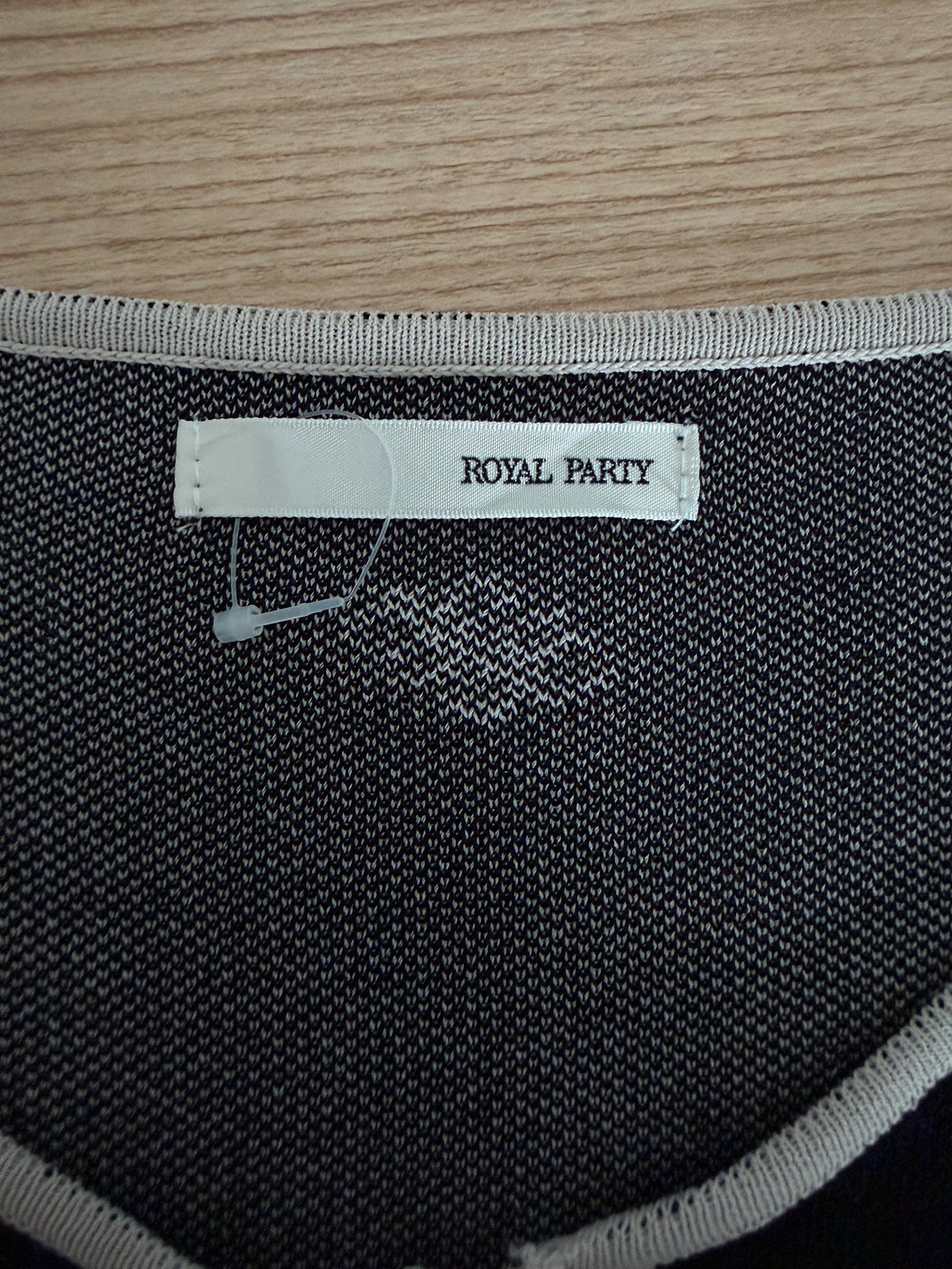 Close-up of a knit garment neck label reading ROYAL PARTY, showing a dark charcoal-gray fabric with light gray trim on a wood surface.