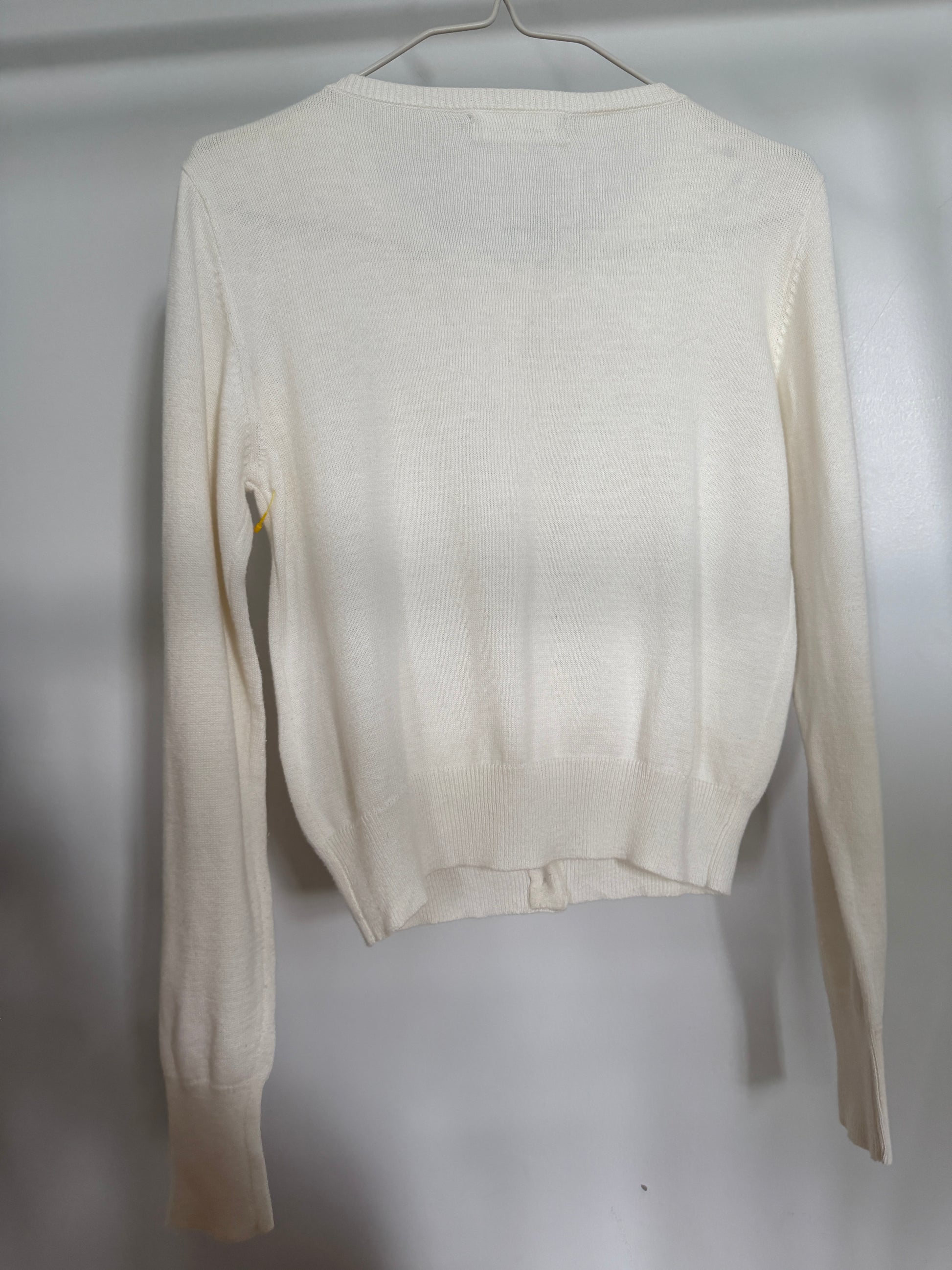 An off-white knit long-sleeve sweater hanging on a metal hanger against a light gray wall.