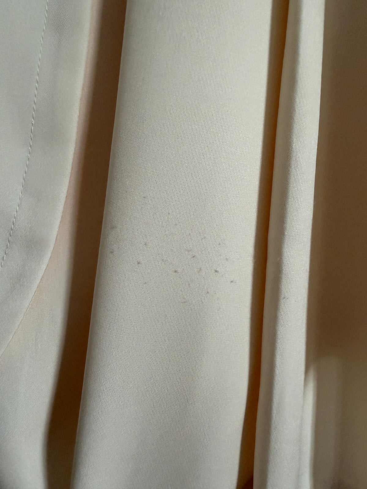 Close-up of draped off-white or cream fabric with soft folds and a subtle sheen.