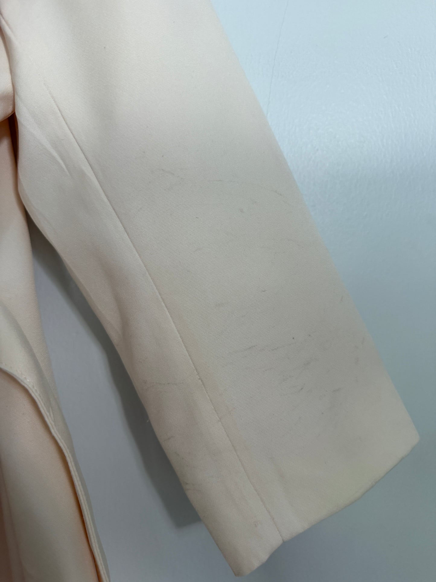 A close-up of a light cream or off-white fabric sleeve, showing fine scuffs and lint on the surface against a pale blue-gray background.