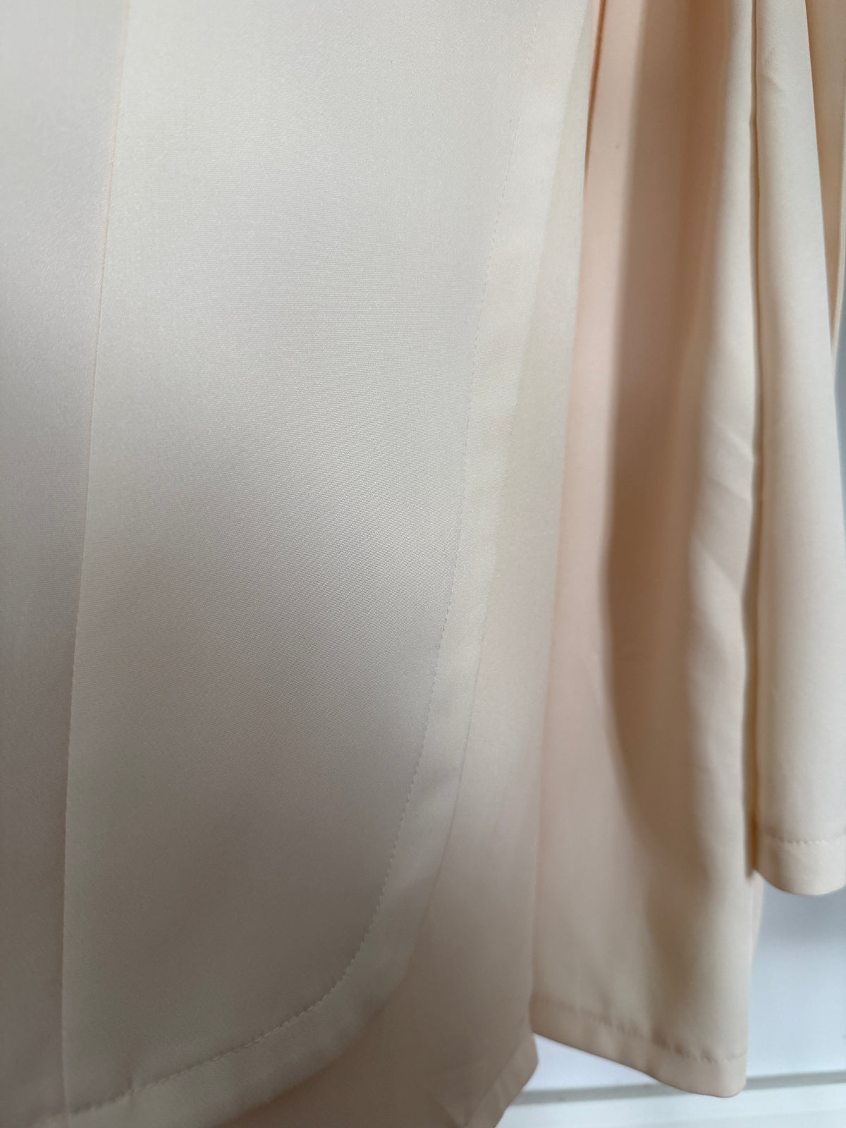 Close-up of a light beige or cream-colored fabric garment, showing the smooth texture and soft folds of the material.