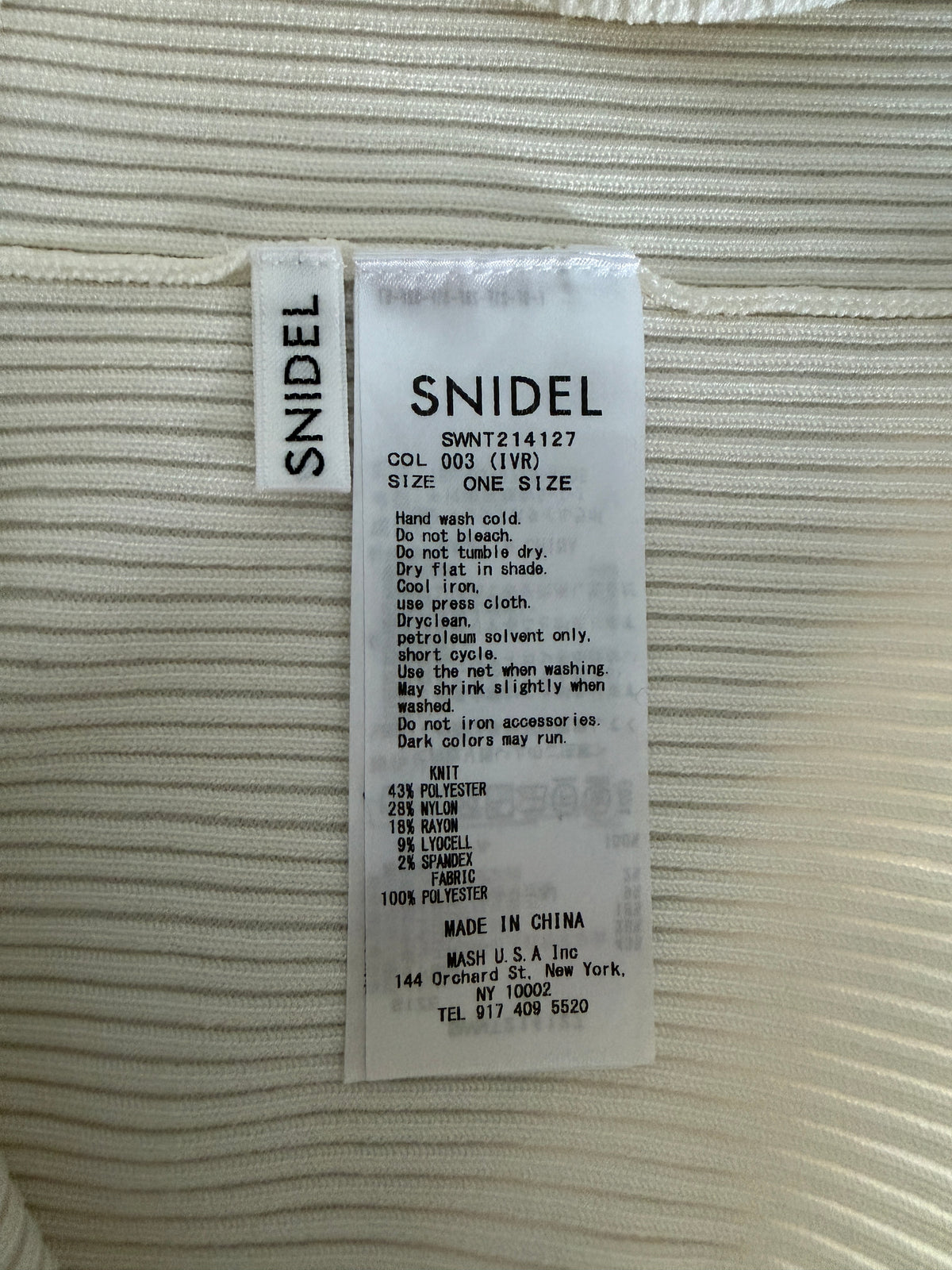 A close-up of a ribbed cream-colored garment showing the interior tag, which is labeled 'SNIDEL'. The tag contains product details including color, size, and care instructions.