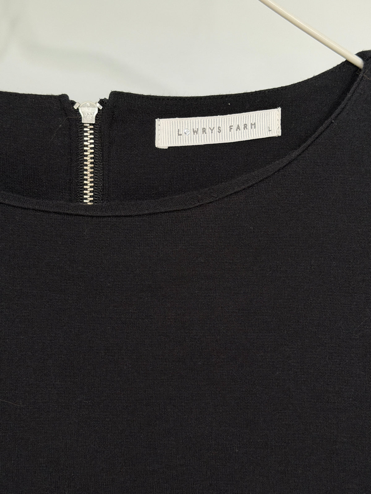 Close-up of a black knit top on a hanger, showing a silver zipper at the neckline and a white fabric label reading 'LINNSYF FARM'.
