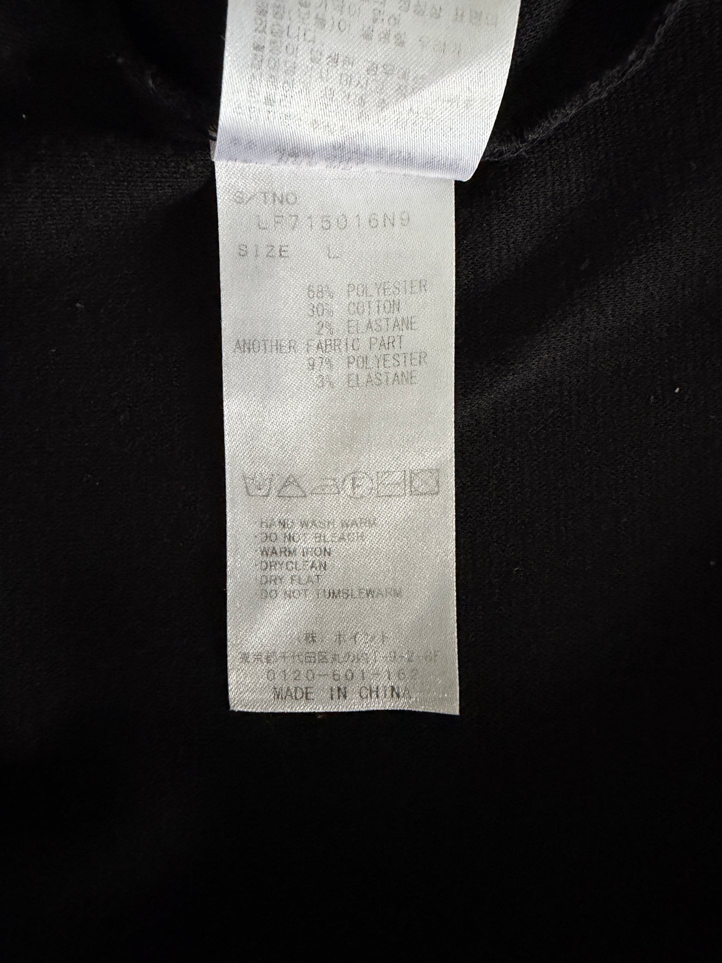 A close-up of a white garment care and size tag sewn onto a black fabric garment. The tag contains printed text with size information and care symbols, including 'MADE IN CHINA'.