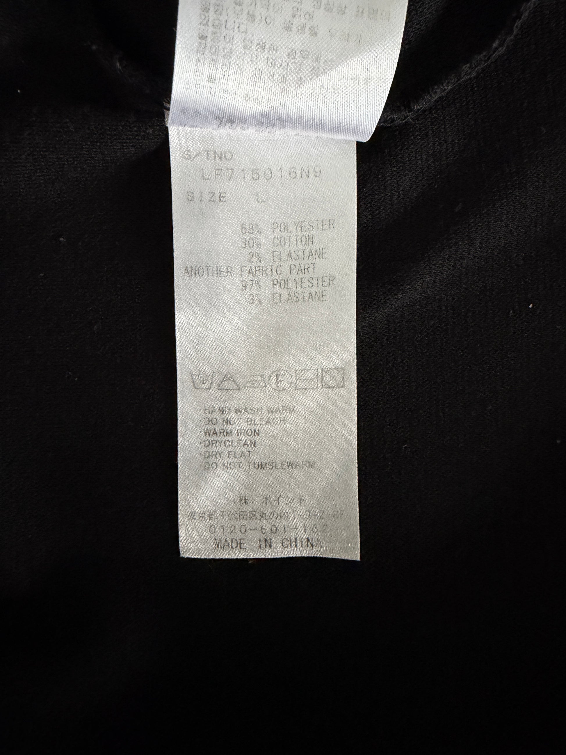 A close-up of a white garment care and size tag sewn onto a black fabric garment. The tag contains printed text with size information and care symbols, including 'MADE IN CHINA'.