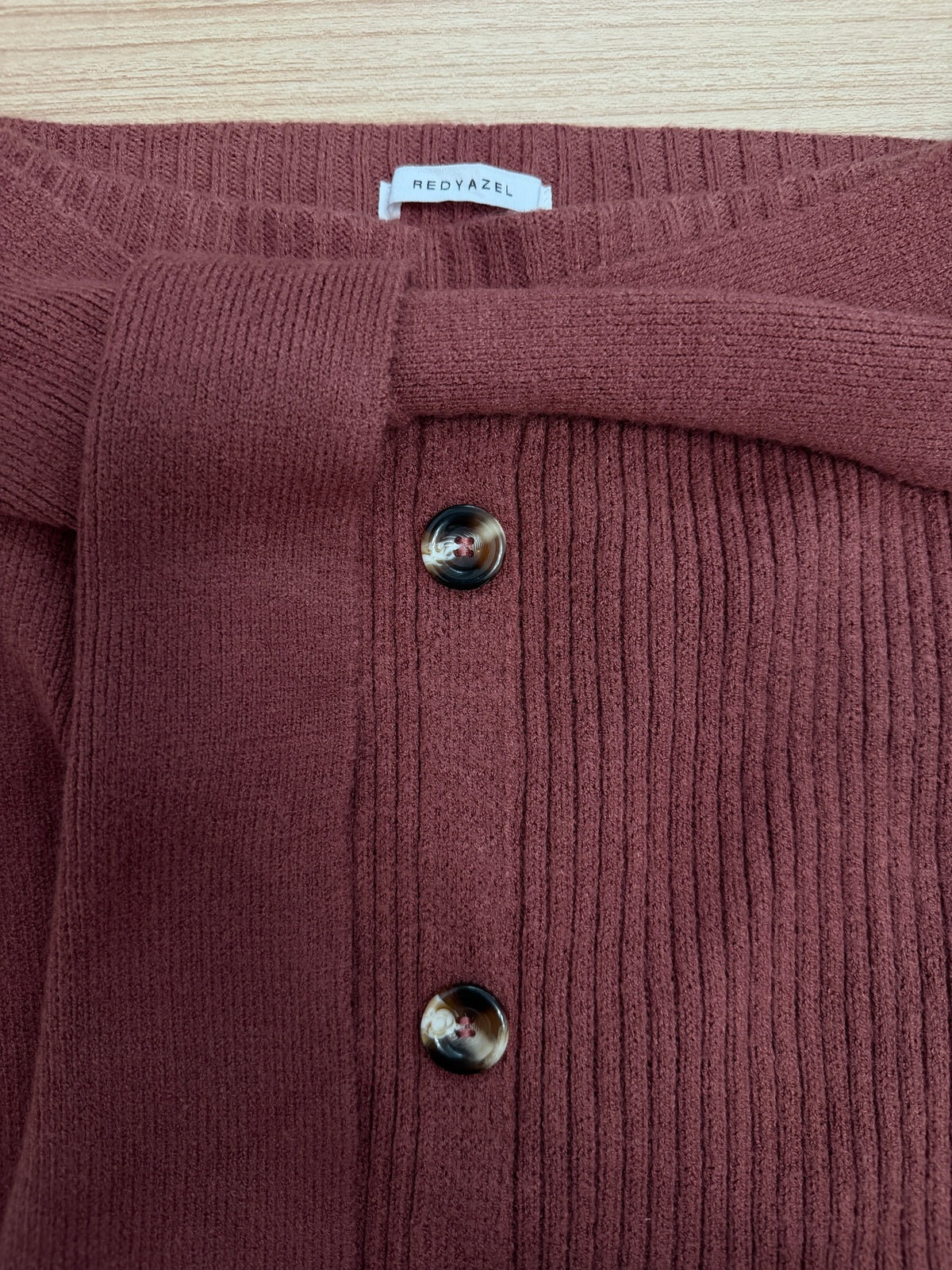 Close-up of a ribbed knit cardigan in a dusty rose or mauve color, featuring two dark metallic buttons and a white neck label reading 'NEOFAZEL'.