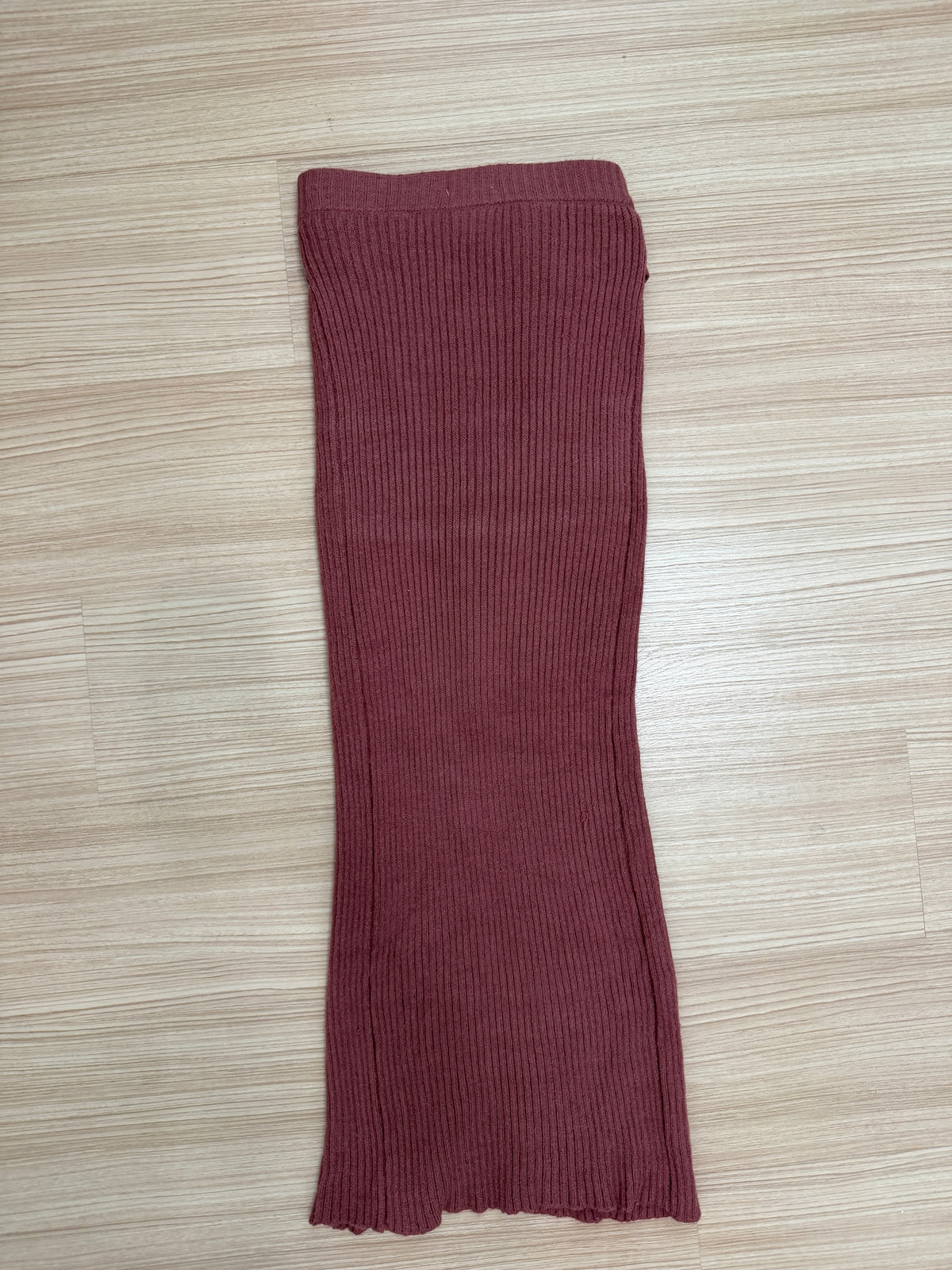 A ribbed knit sleeveless top or long tube top in a dusty burgundy red, laid flat on a light wood floor.