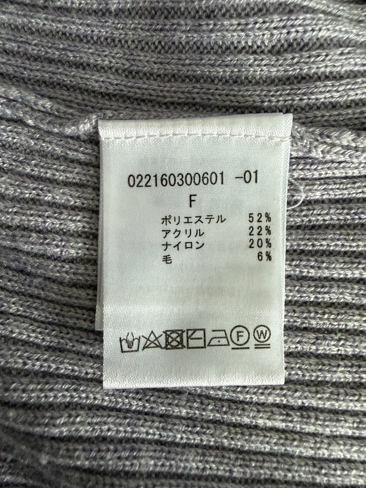 A close-up of a gray ribbed knit garment showing a white fabric care label with Japanese text and care symbols.