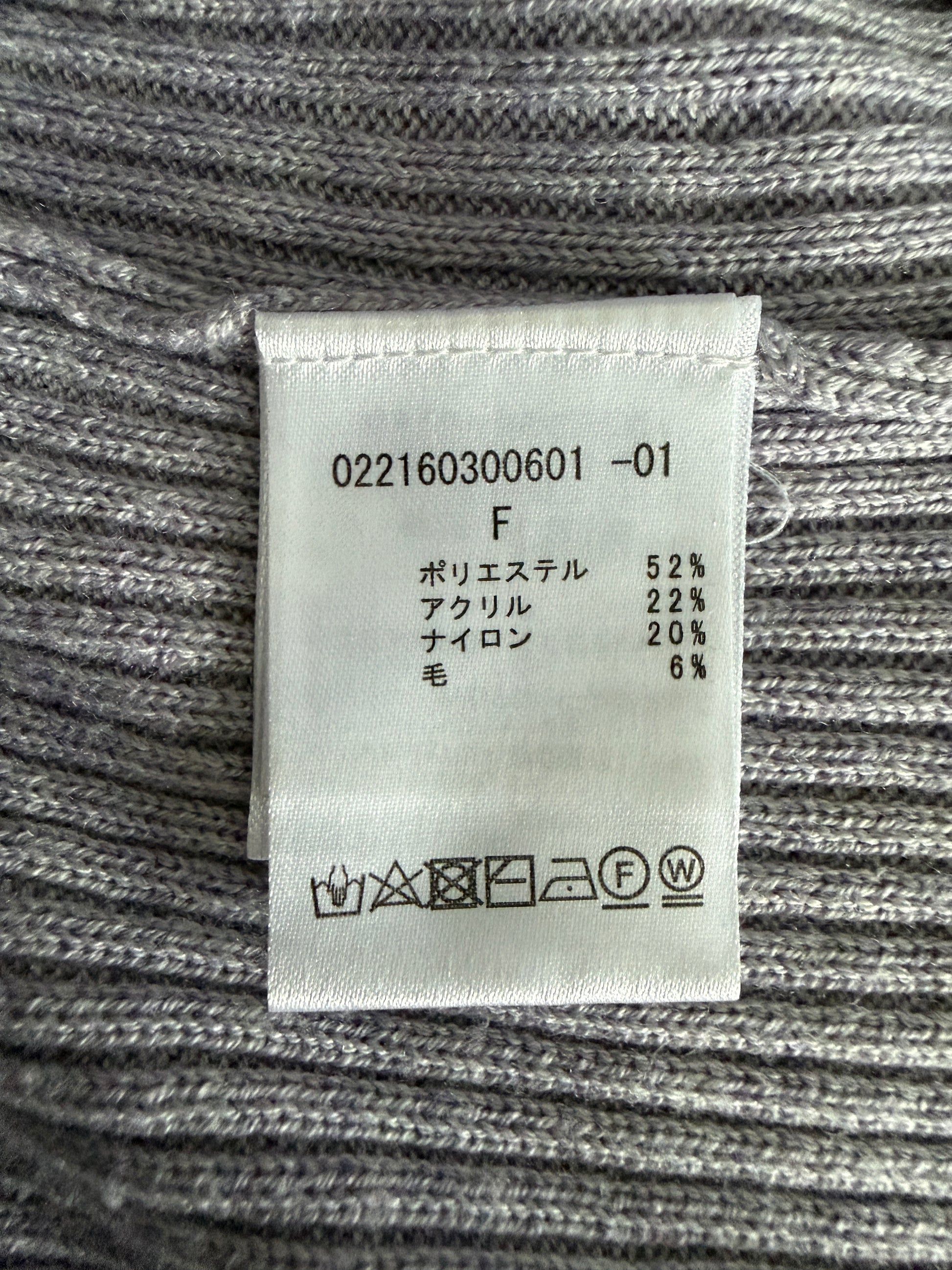 A close-up of a gray ribbed knit garment showing a white fabric care label with Japanese text and care symbols.