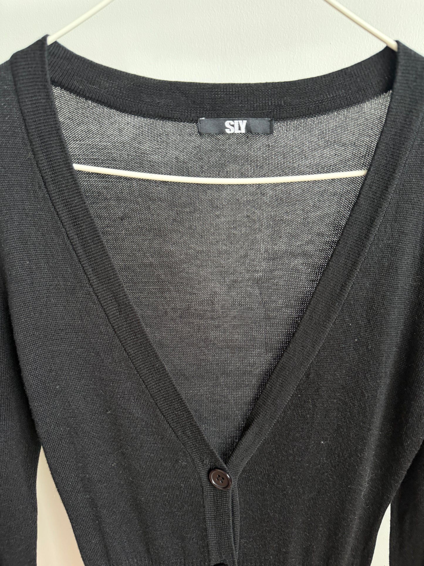 A close-up of a dark gray knit cardigan sweater hanging on a white hanger, showing a V-neckline, ribbed collar, and a small button closure.