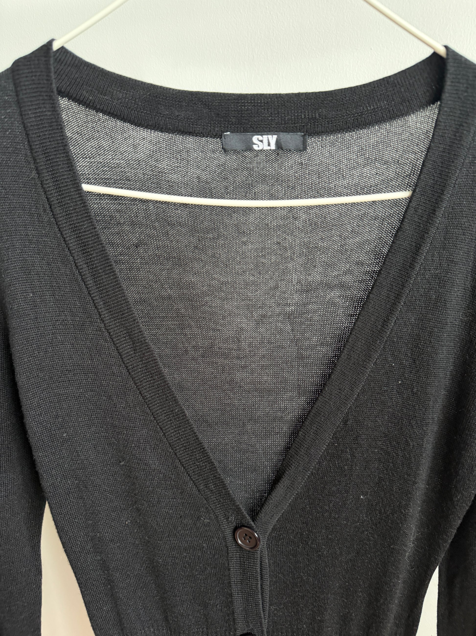 A close-up of a dark gray knit cardigan sweater hanging on a white hanger, showing a V-neckline, ribbed collar, and a small button closure.