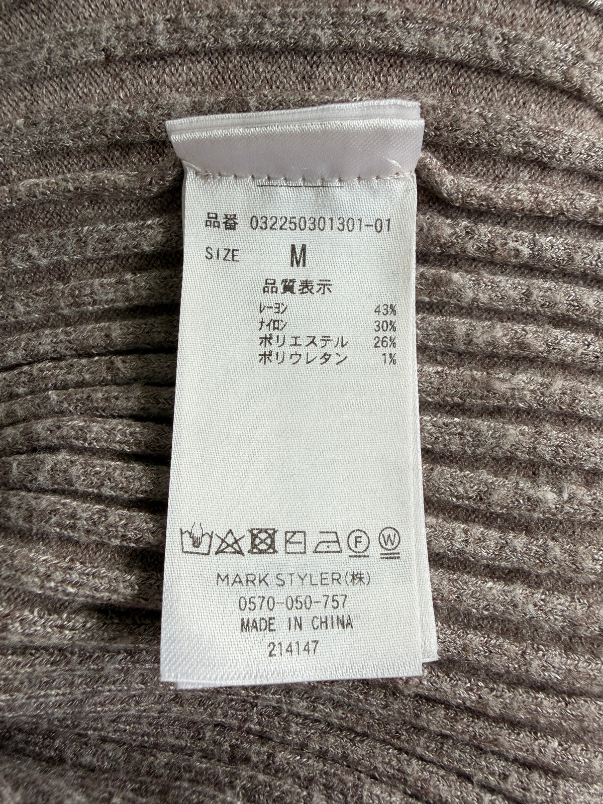 A close-up of a white garment size and care label sewn onto ribbed gray fabric.