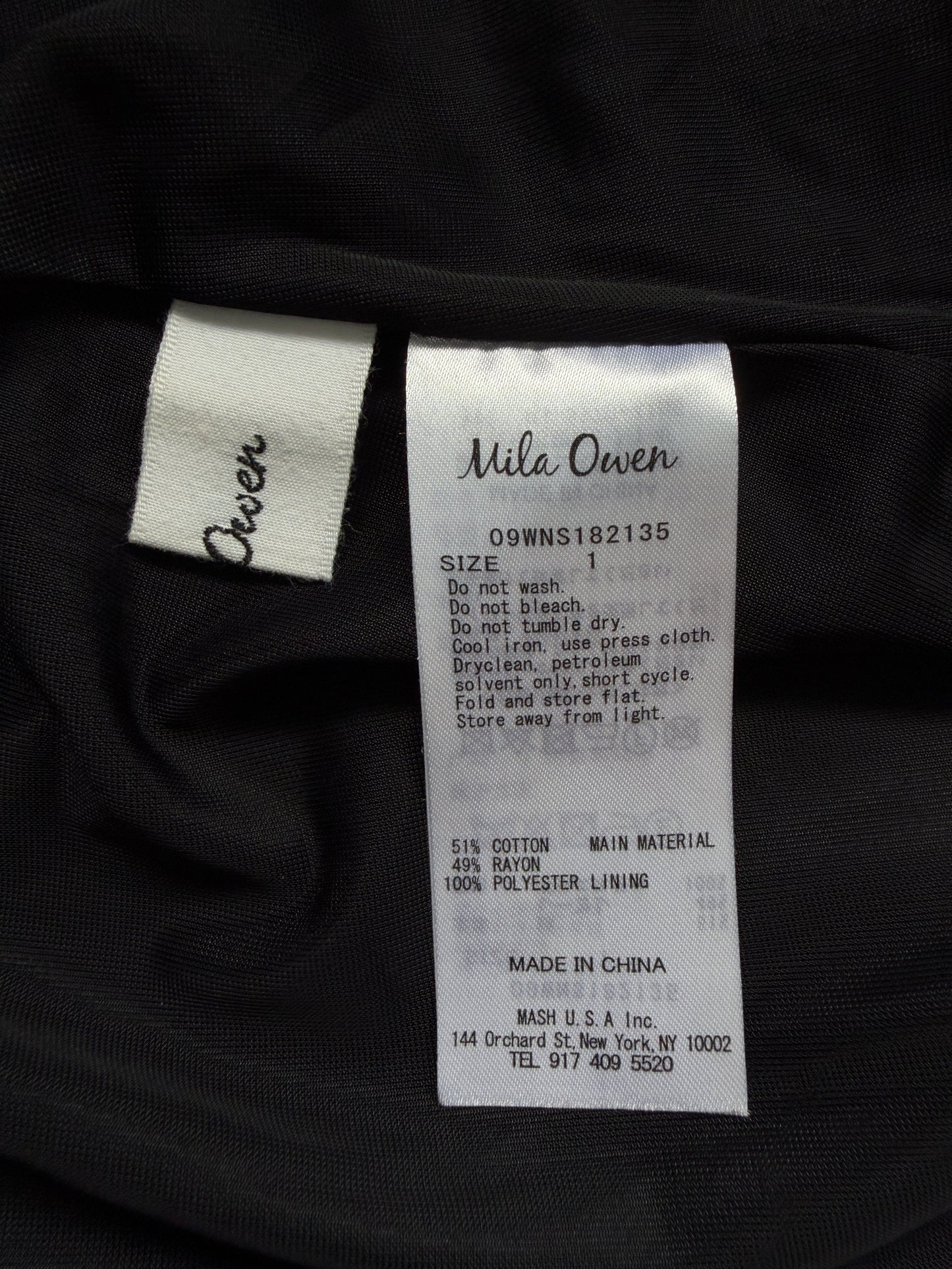 Close-up of a garment's interior labels showing the brand 'Mila Owen' on a white sewn-in tag and 'Owen' on a matching fabric tag, with size information printed on the main label.