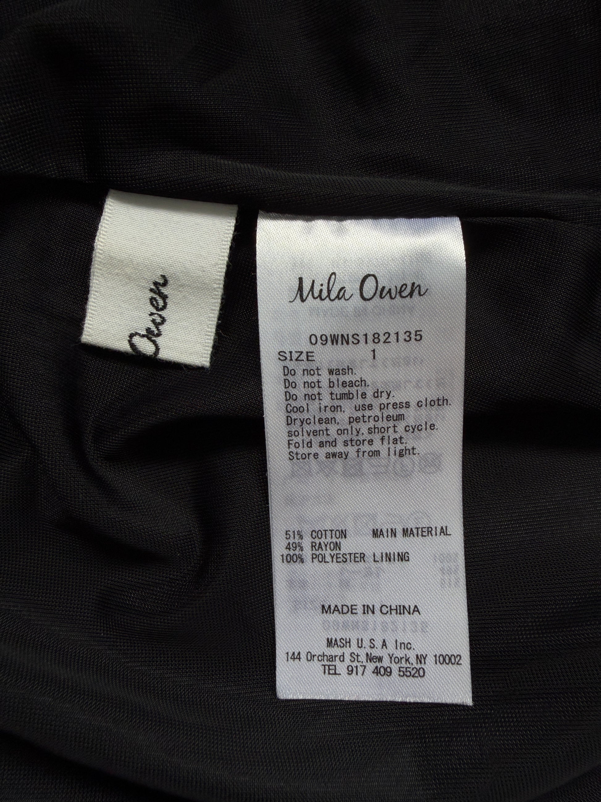 Close-up of a garment's interior labels showing the brand 'Mila Owen' on a white sewn-in tag and 'Owen' on a matching fabric tag, with size information printed on the main label.