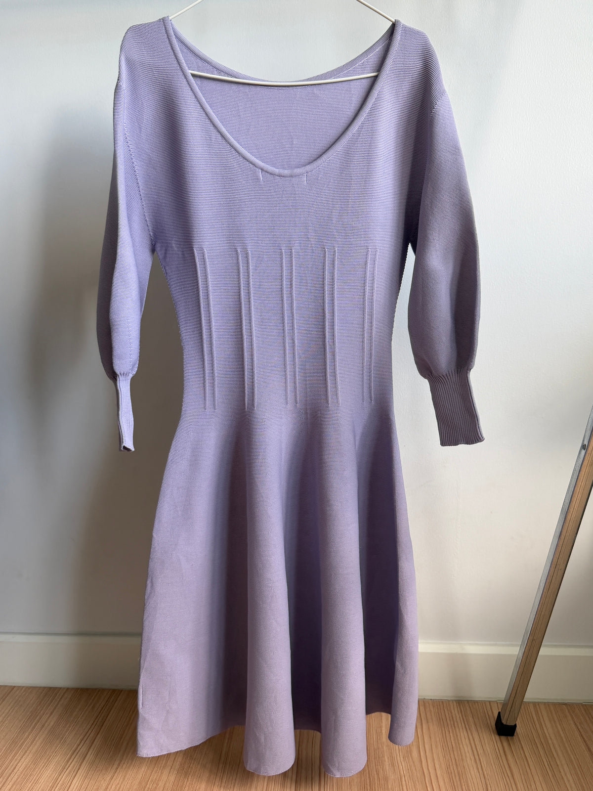 A lavender purple knit dress with three-quarter sleeves and a scoop neckline, hanging on a white hanger against a plain wall.