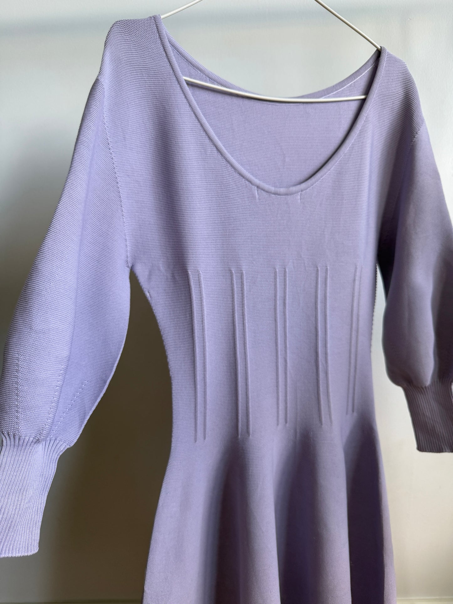 A lavender purple knit sweater dress with a scoop neckline, 3/4 sleeves, and vertical ribbed details on the bodice, hanging on a metal hanger against a plain light background.