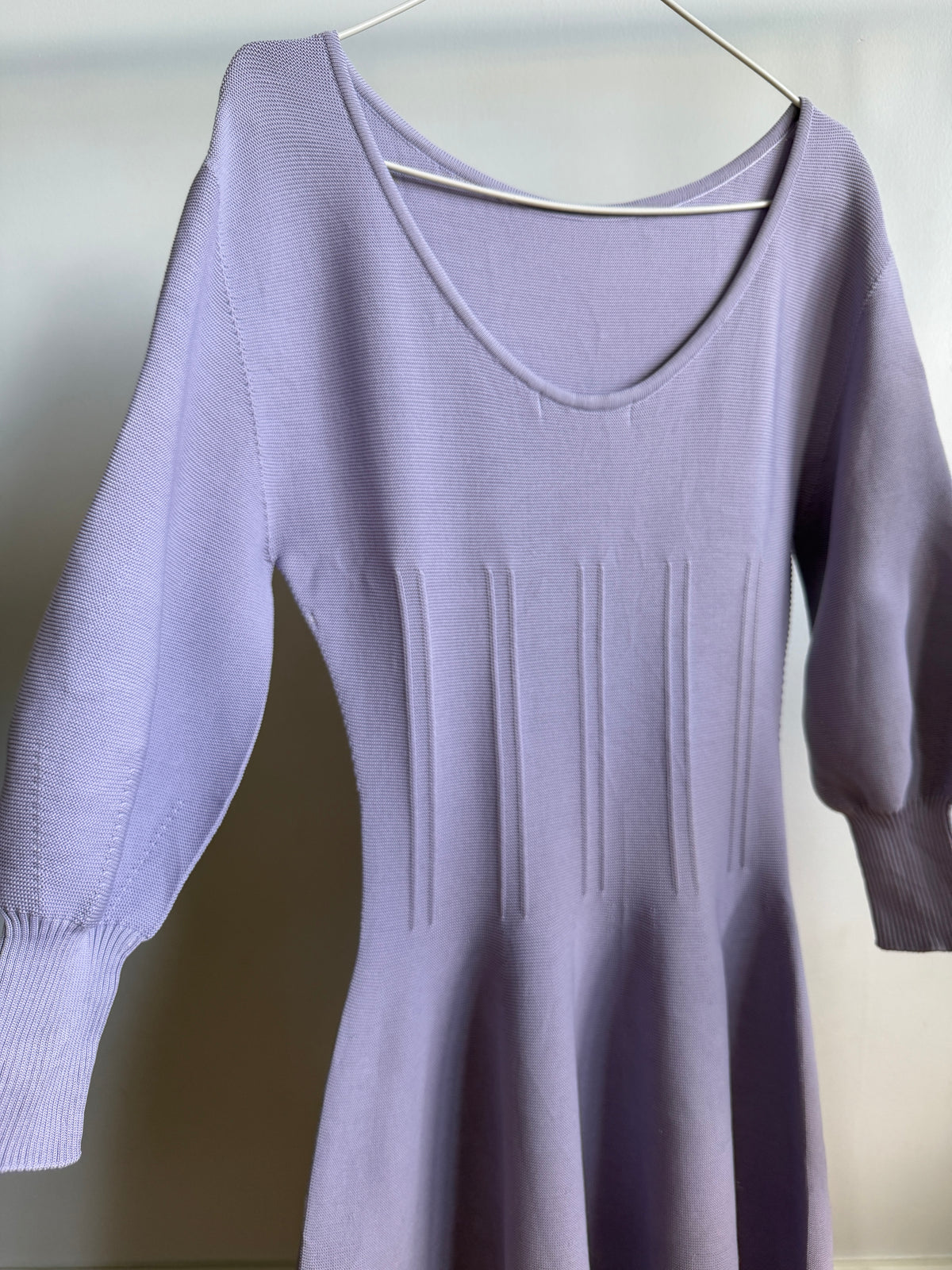 A lavender purple knit sweater dress with a scoop neckline, 3/4 sleeves, and vertical ribbed details on the bodice, hanging on a metal hanger against a plain light background.