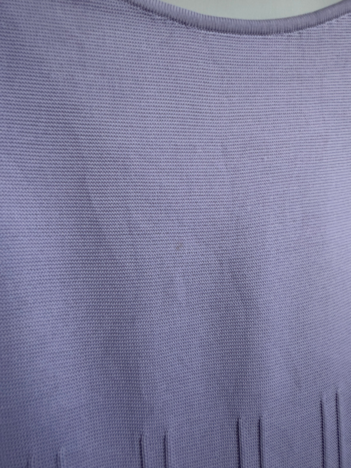 Close-up of a lavender purple knit fabric texture, showing the fine woven pattern and a small portion of a vertical slit neckline.