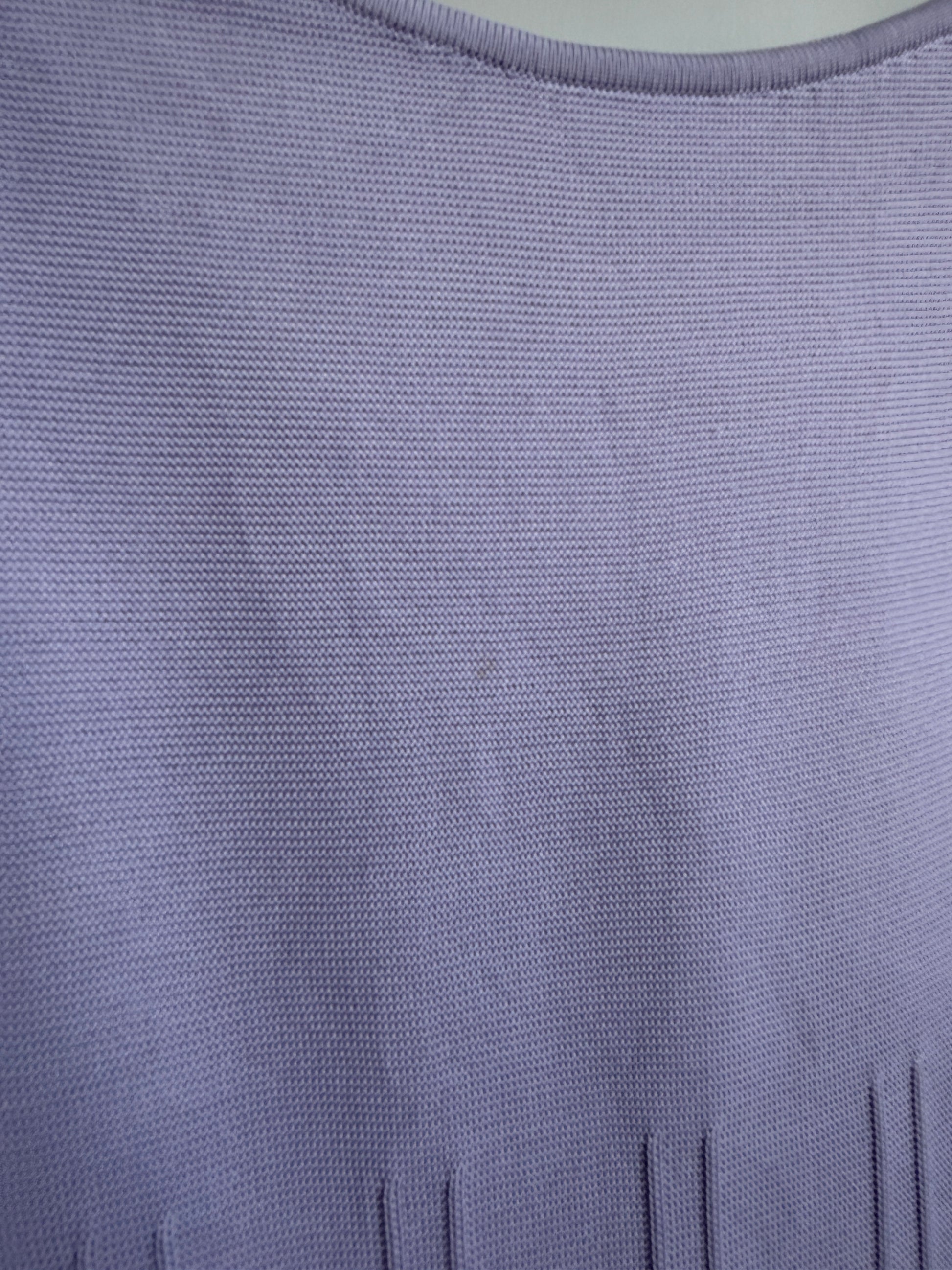 Close-up of a lavender purple knit fabric texture, showing the fine woven pattern and a small portion of a vertical slit neckline.
