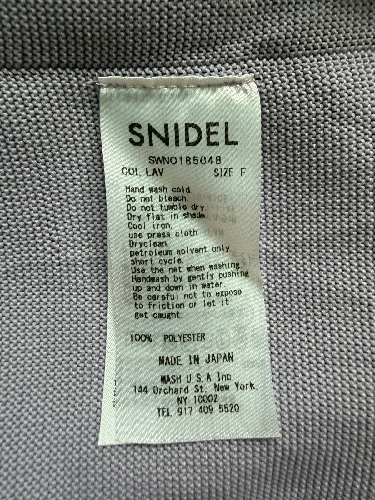 A close-up of a white fabric care label reading 'SNIDEL' with care instructions and 'MADE IN JAPAN' on a gray woven textile background.