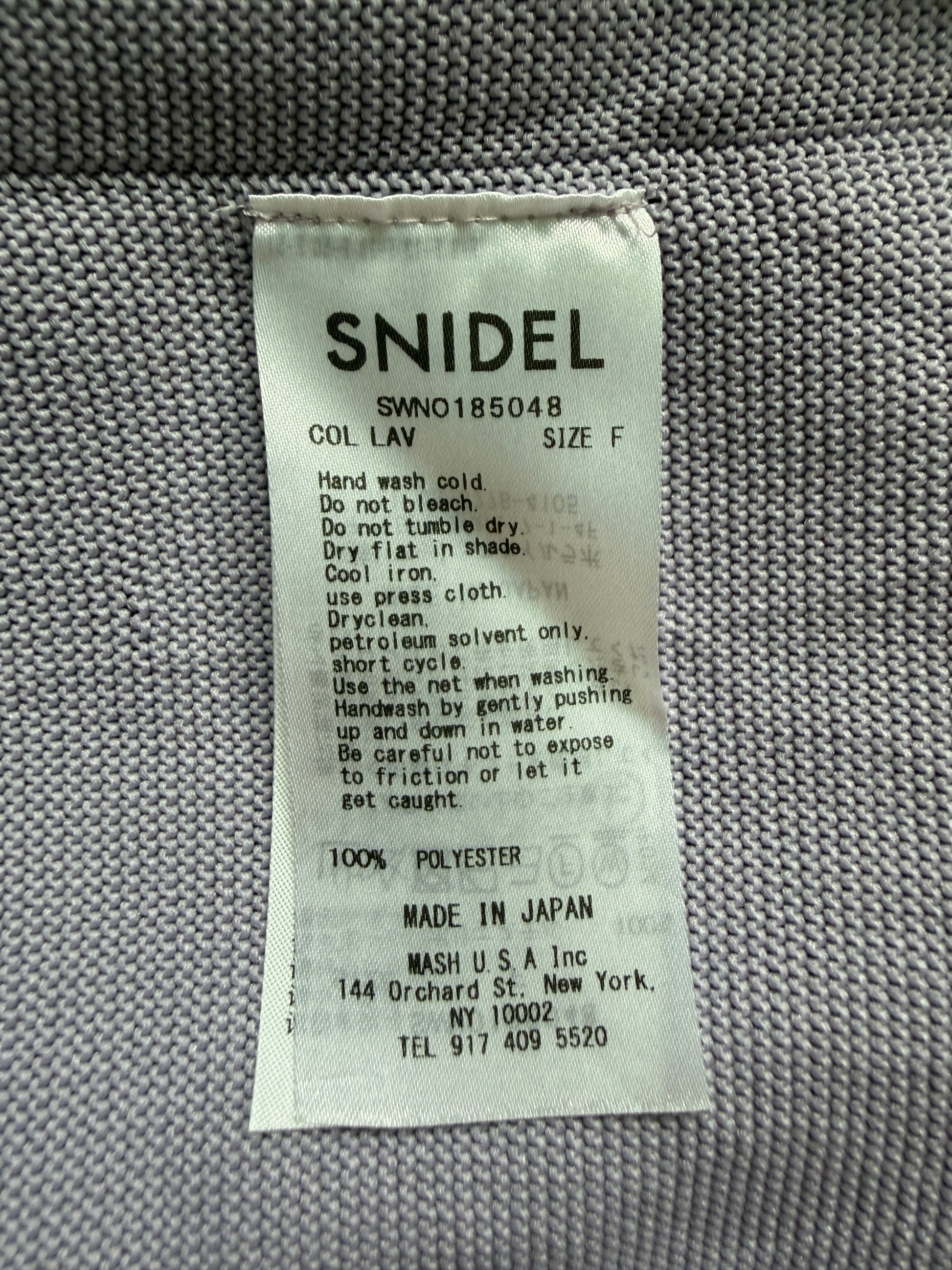 A close-up of a white fabric care label reading 'SNIDEL' with care instructions and 'MADE IN JAPAN' on a gray woven textile background.