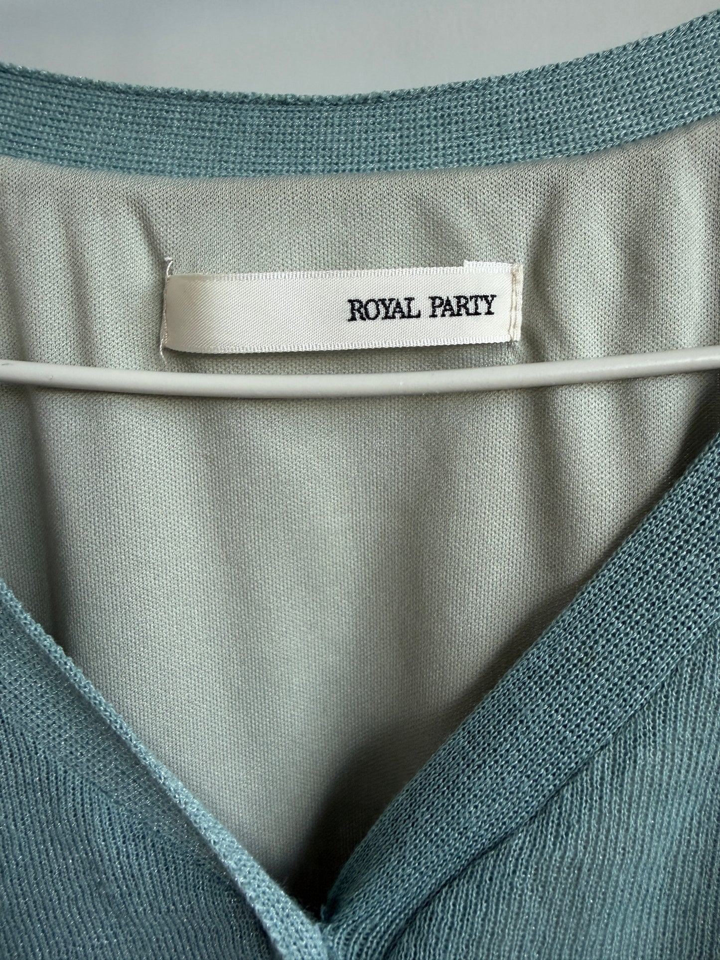 Close-up of a knit top or sweater collar with a visible neck label reading ROYAL PARTY. The garment has a muted blue-green/teal knit exterior and a lighter sage-gray interior lining, shown hanging against a neutral gray background.