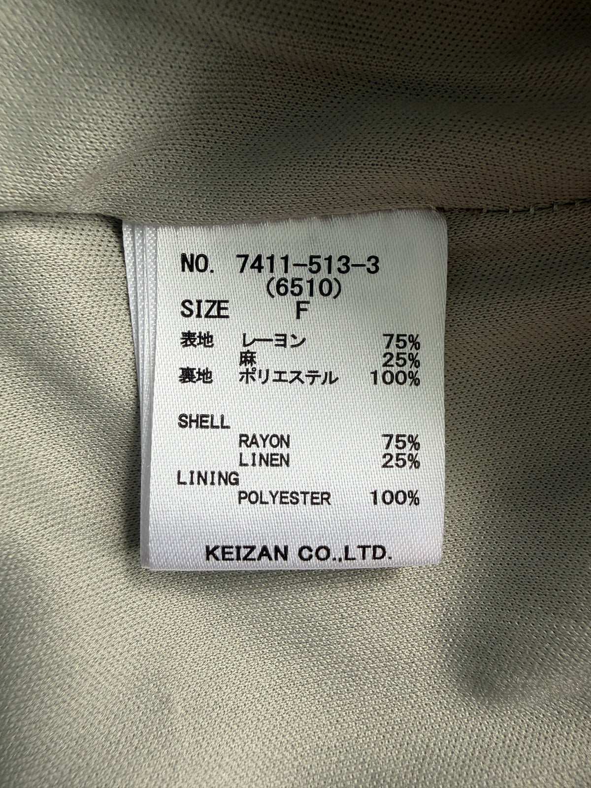 A close-up of a garment's interior size and material label reading 'SIZE F' with composition, shell, linen, and polyester percentages, plus the brand 'KEIZAN CO.,LTD.