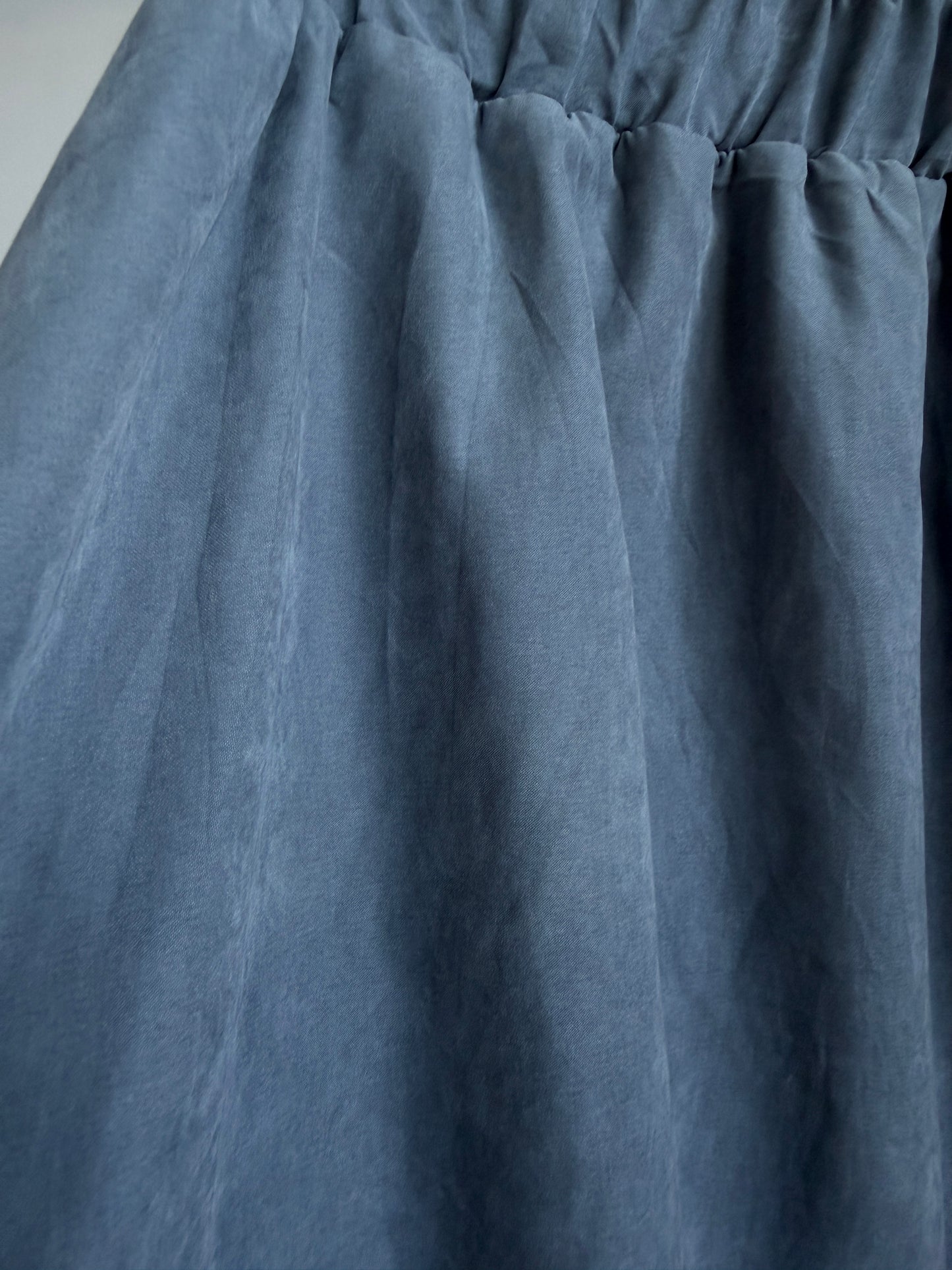 A close-up of a dusty slate blue fabric, showing the texture and gathered waist seam of a garment.