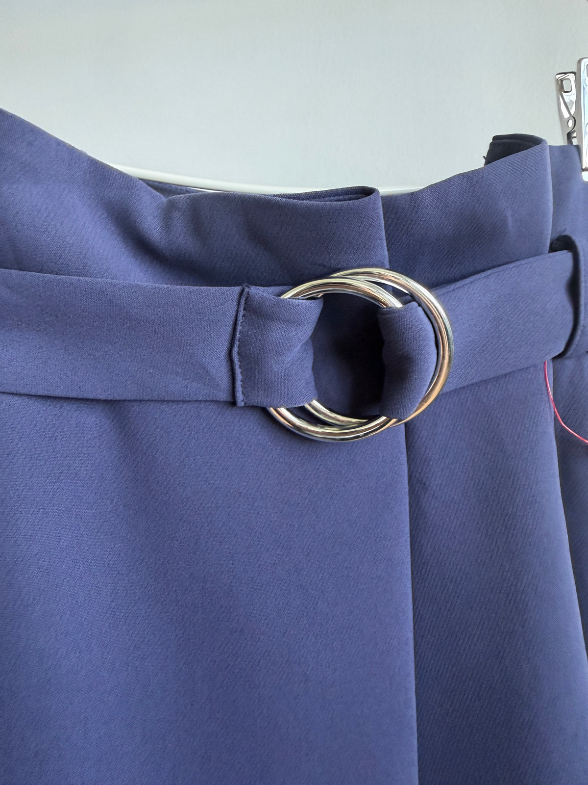 Close-up of a blue waistcoat or skirt with a wide waist belt and a large silver-tone double-ring metal buckle.