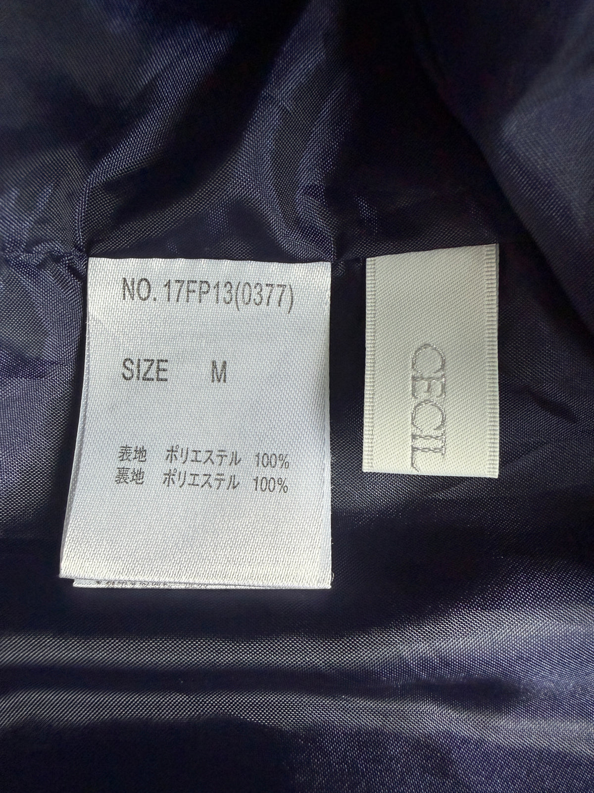 Close-up of a garment's interior labels on dark navy fabric. One white label reads 'NO.