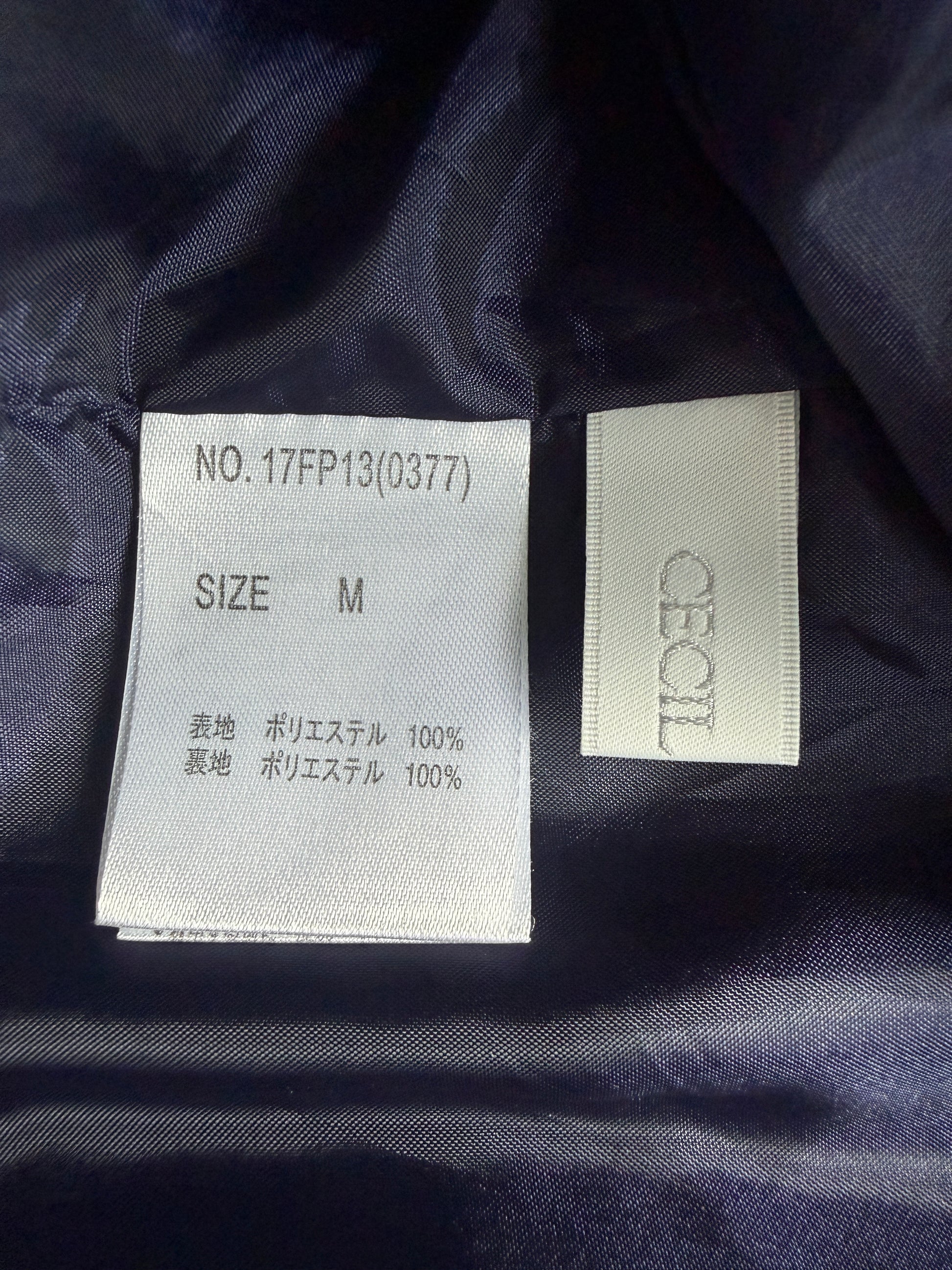 Close-up of a garment's interior labels on dark navy fabric. One white label reads 'NO.