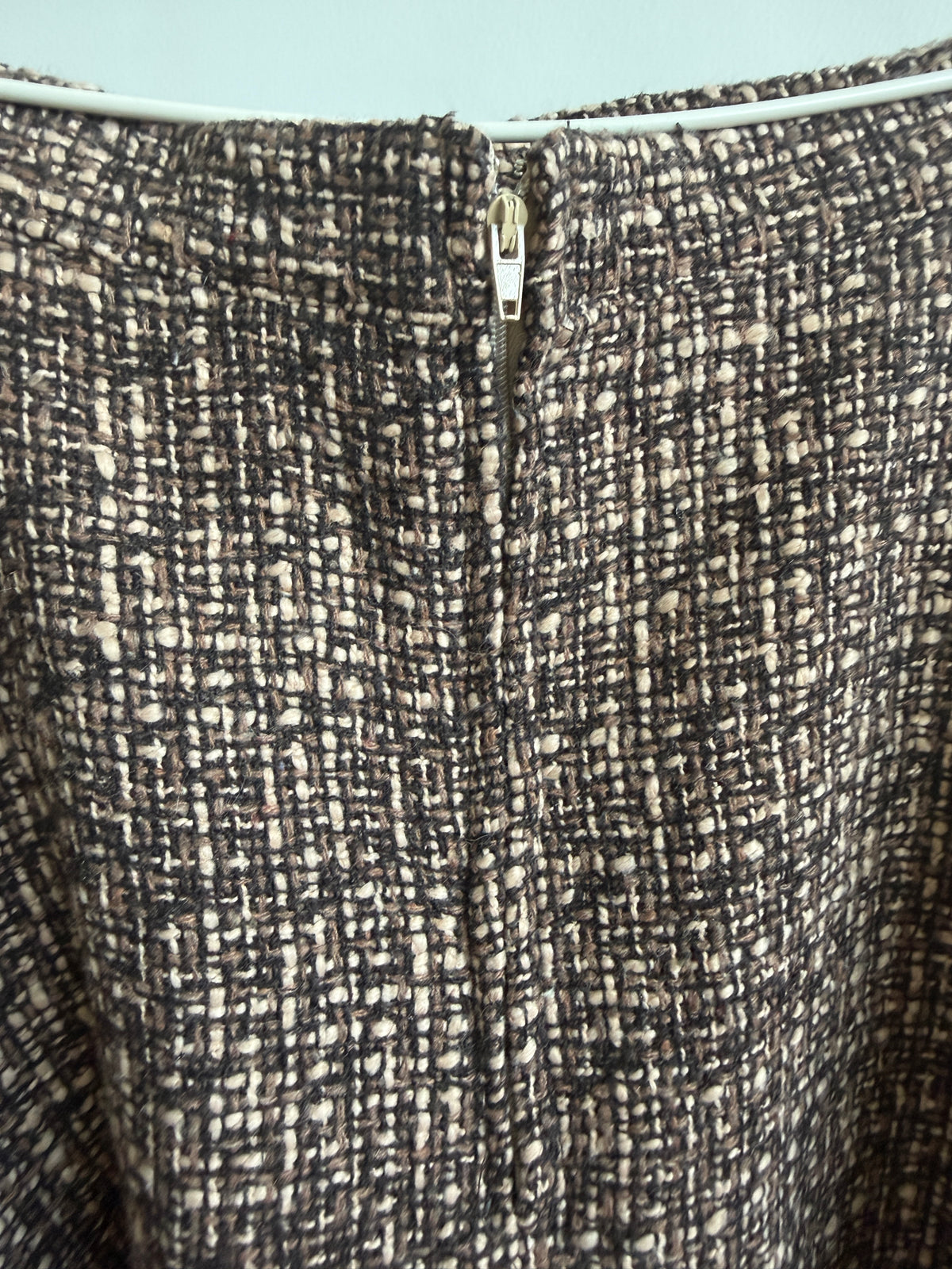 Close-up of a textured tweed fabric garment, showing a black and beige woven pattern with a central zipper.